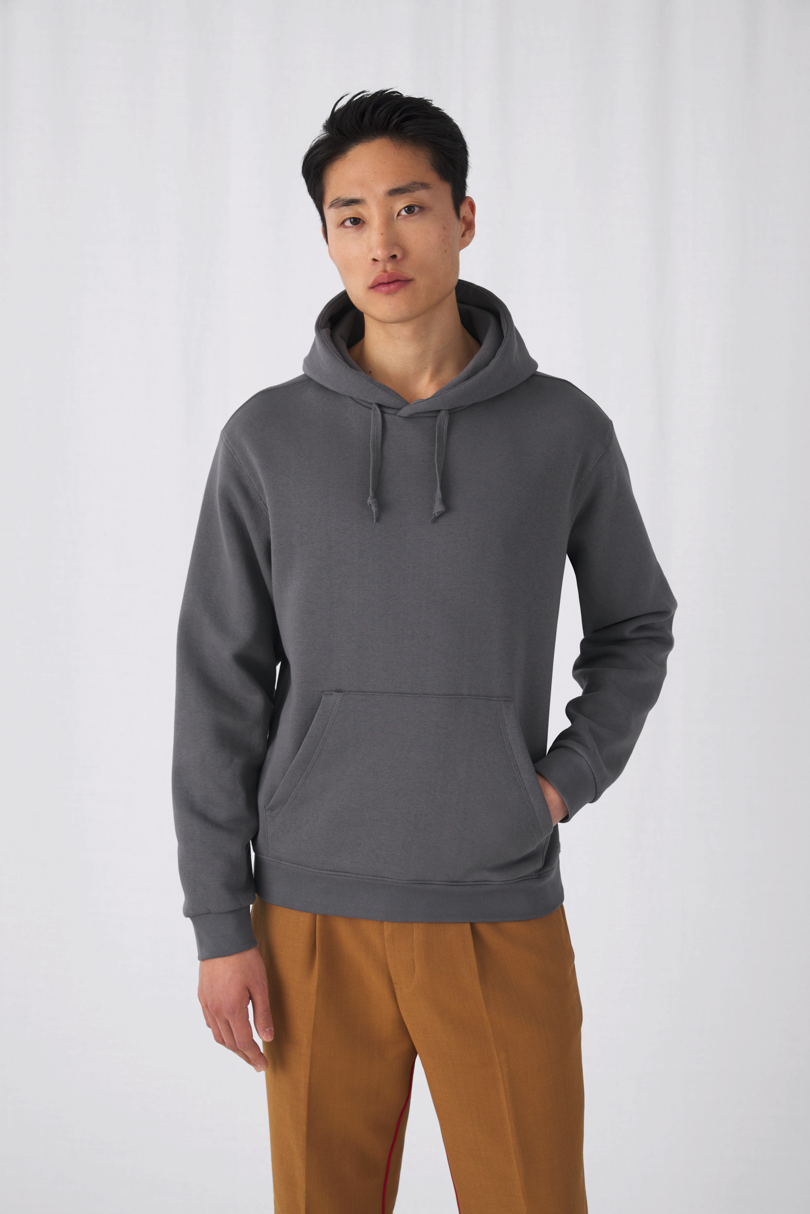 hombre joven con sudadera gris con capucha y pantalones marrón claro sobre fondo blanco