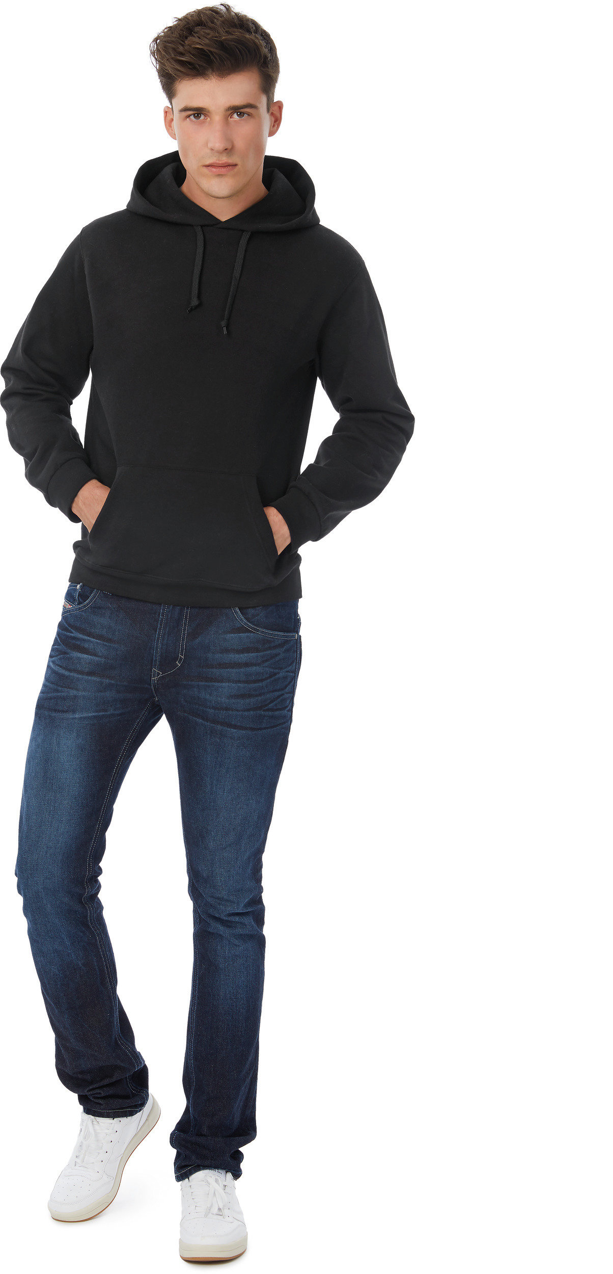 Joven con sudadera negra con capucha, vaqueros y zapatillas blancas sobre fondo blanco.