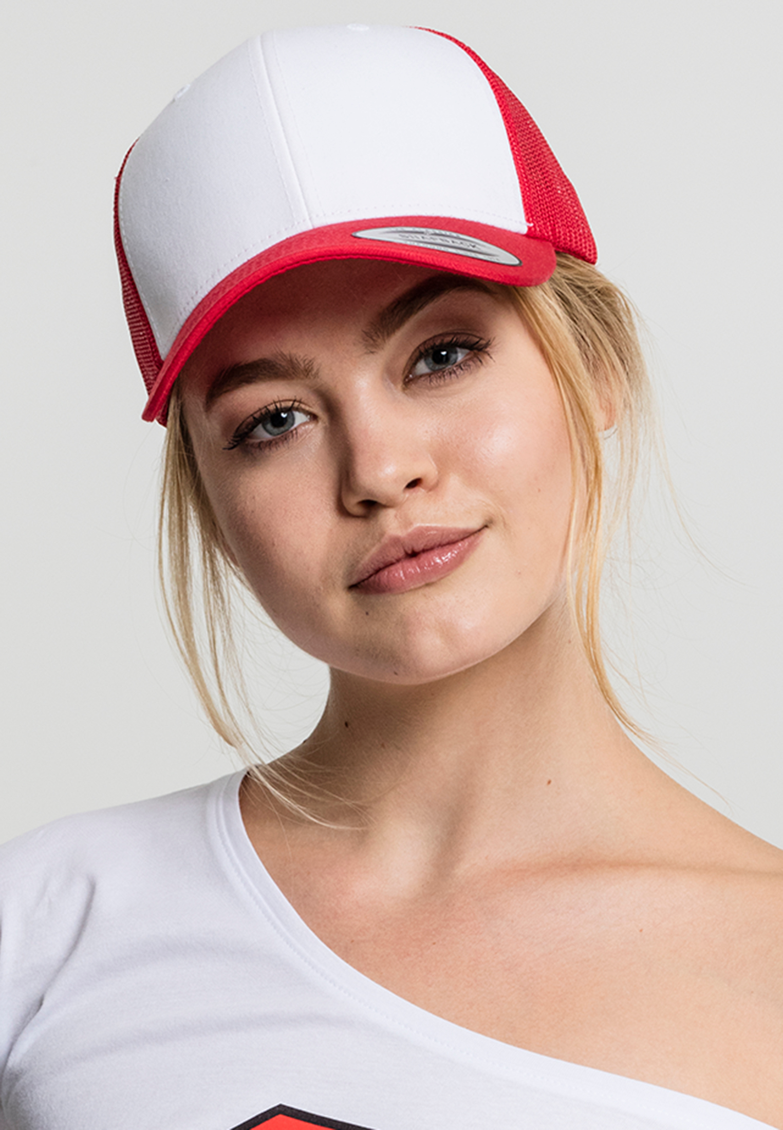 Mujer posando con gorra trucker roja y blanca y camiseta blanca sobre fondo neutro