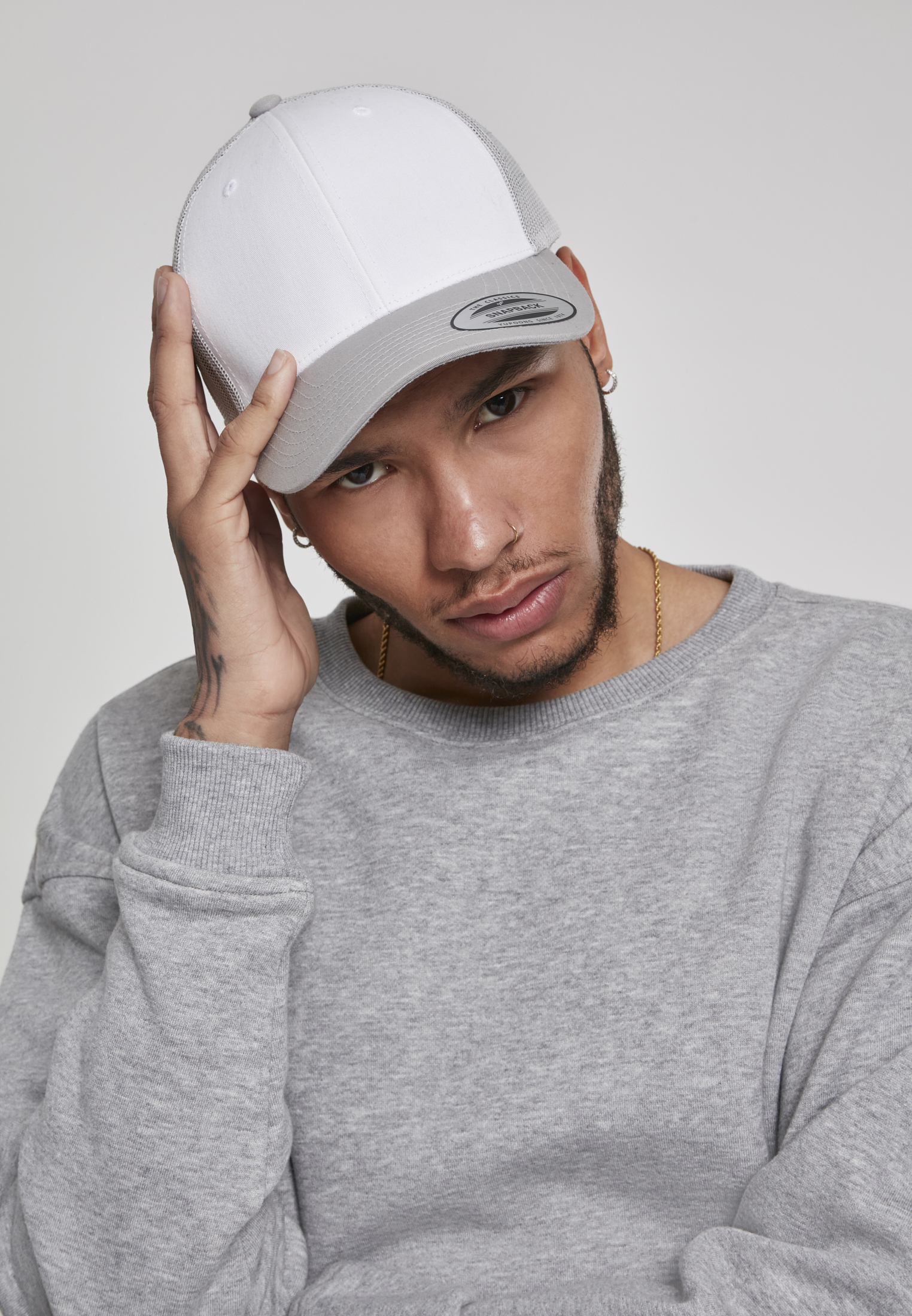 hombre joven con gorra blanca y sudadera gris ajustándose la visera mirando a cámara
