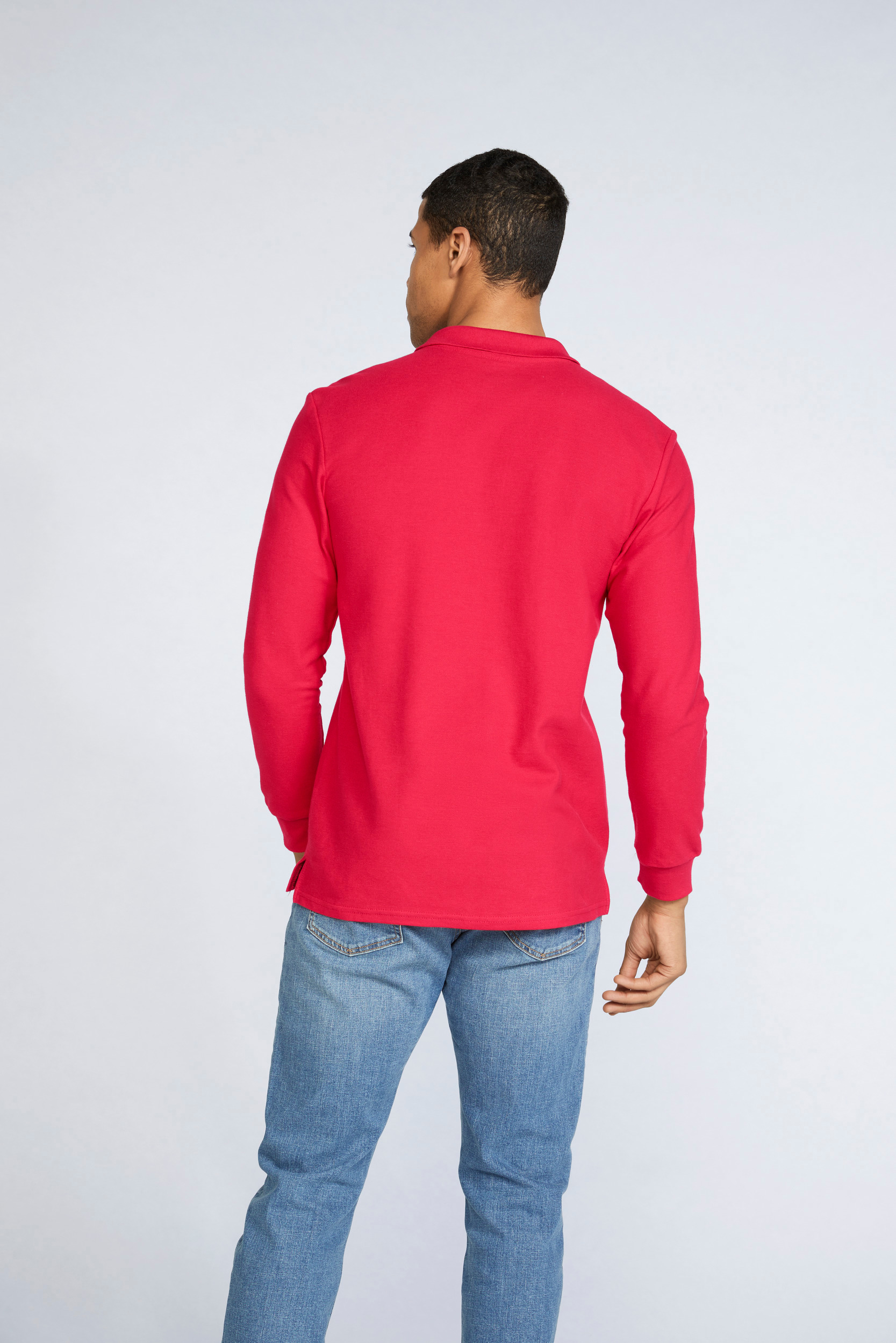 Hombre de espaldas con polo rojo de manga larga y vaqueros claros sobre fondo neutro