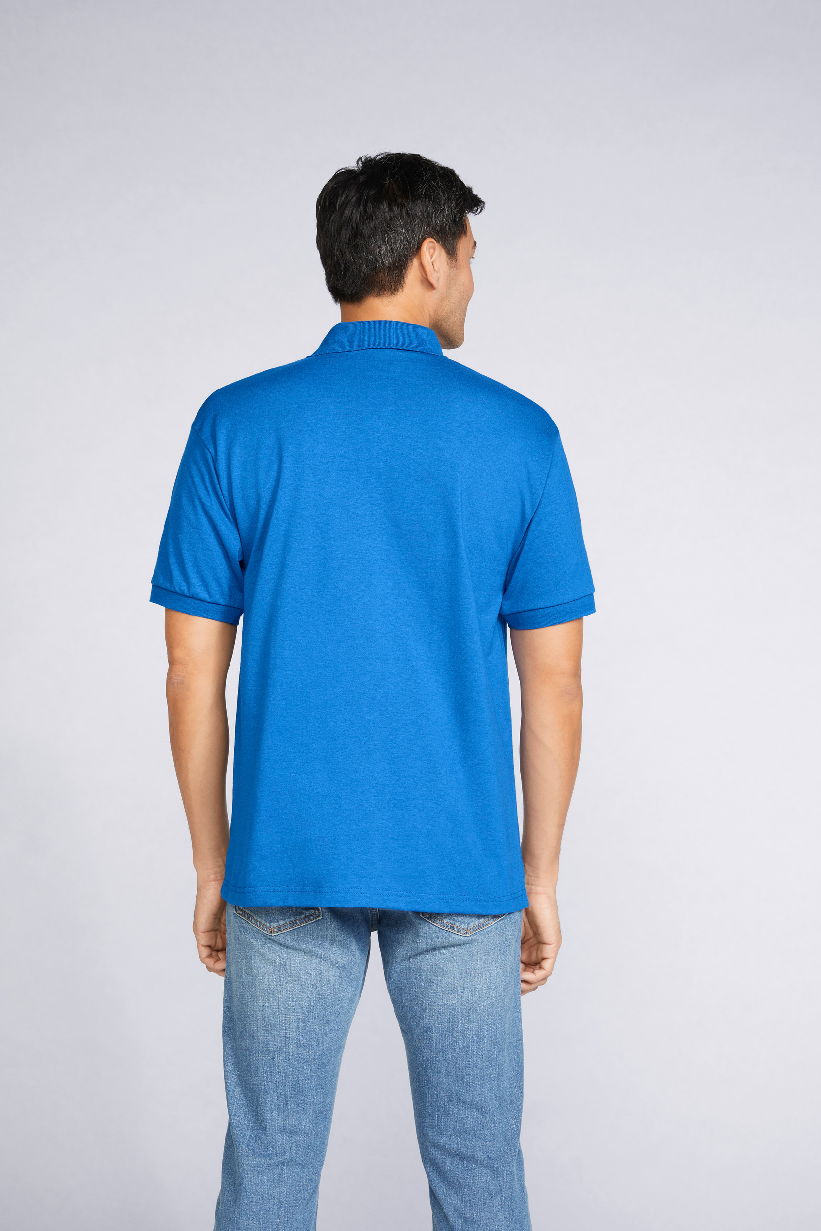 Hombre de espaldas con polo azul y vaqueros sobre fondo neutro.