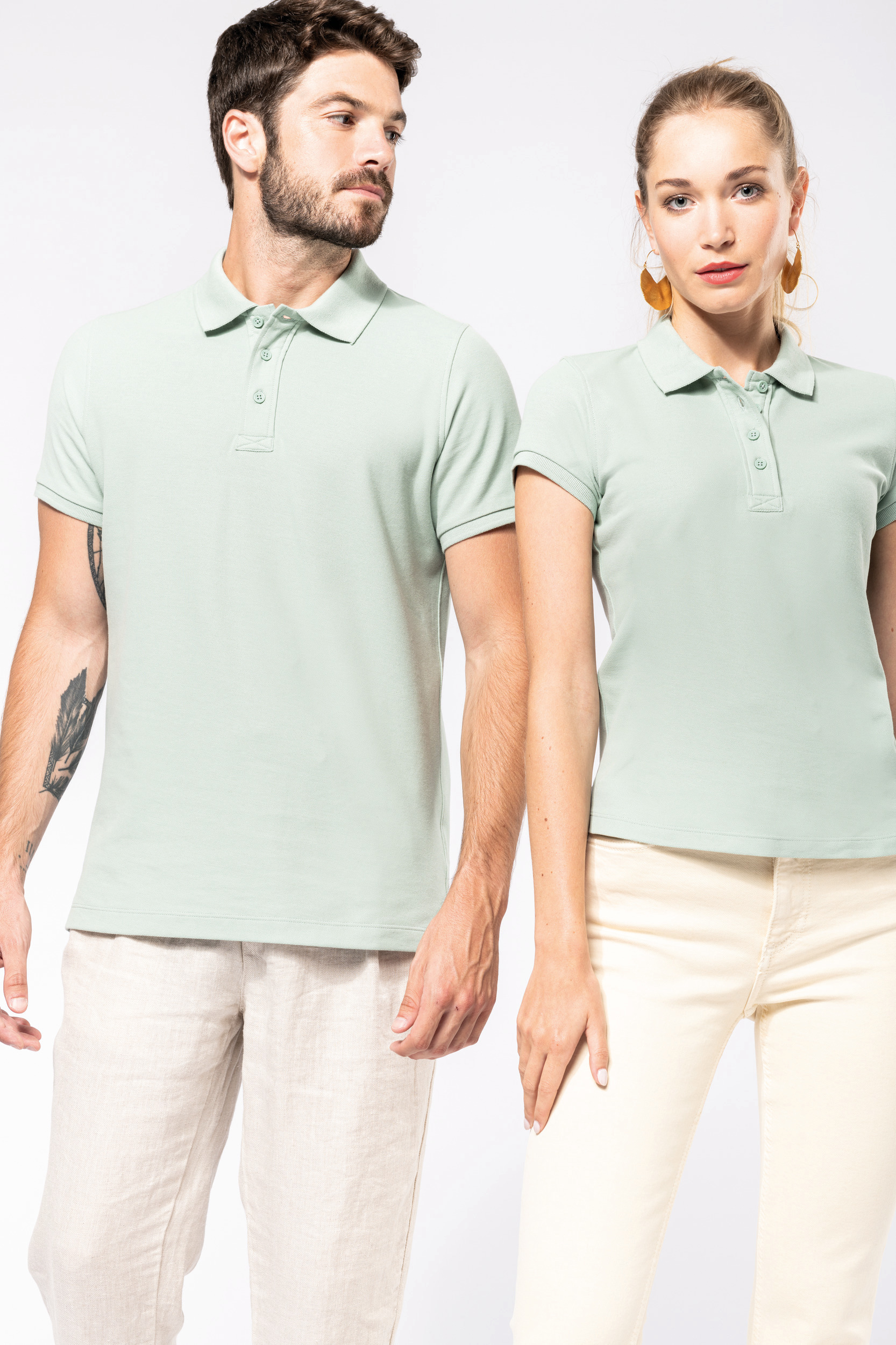 Hombre y mujer de pie con polos verde menta y pantalones claros sobre fondo blanco