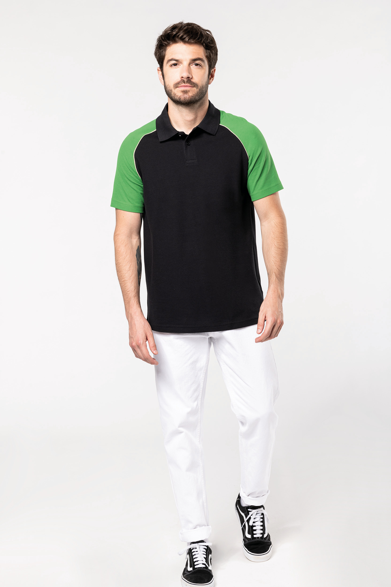 hombre con polo negro de mangas verdes y pantalones blancos en fondo neutro