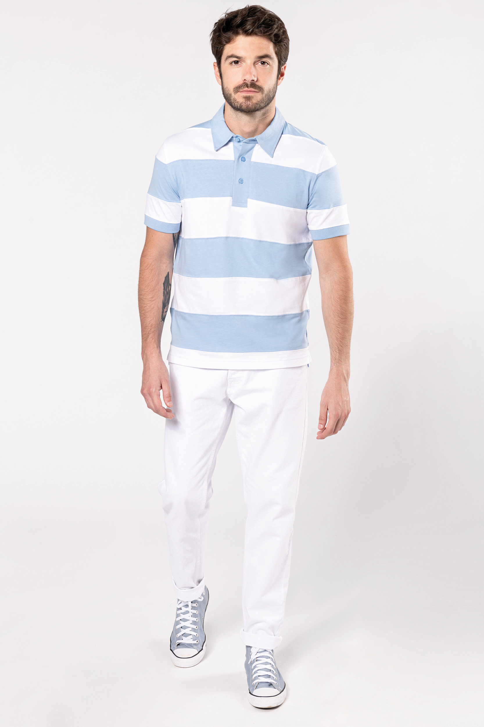 Hombre con polo de rayas azul claro y blanco, pantalón blanco y zapatillas altas azules en estudio minimalista