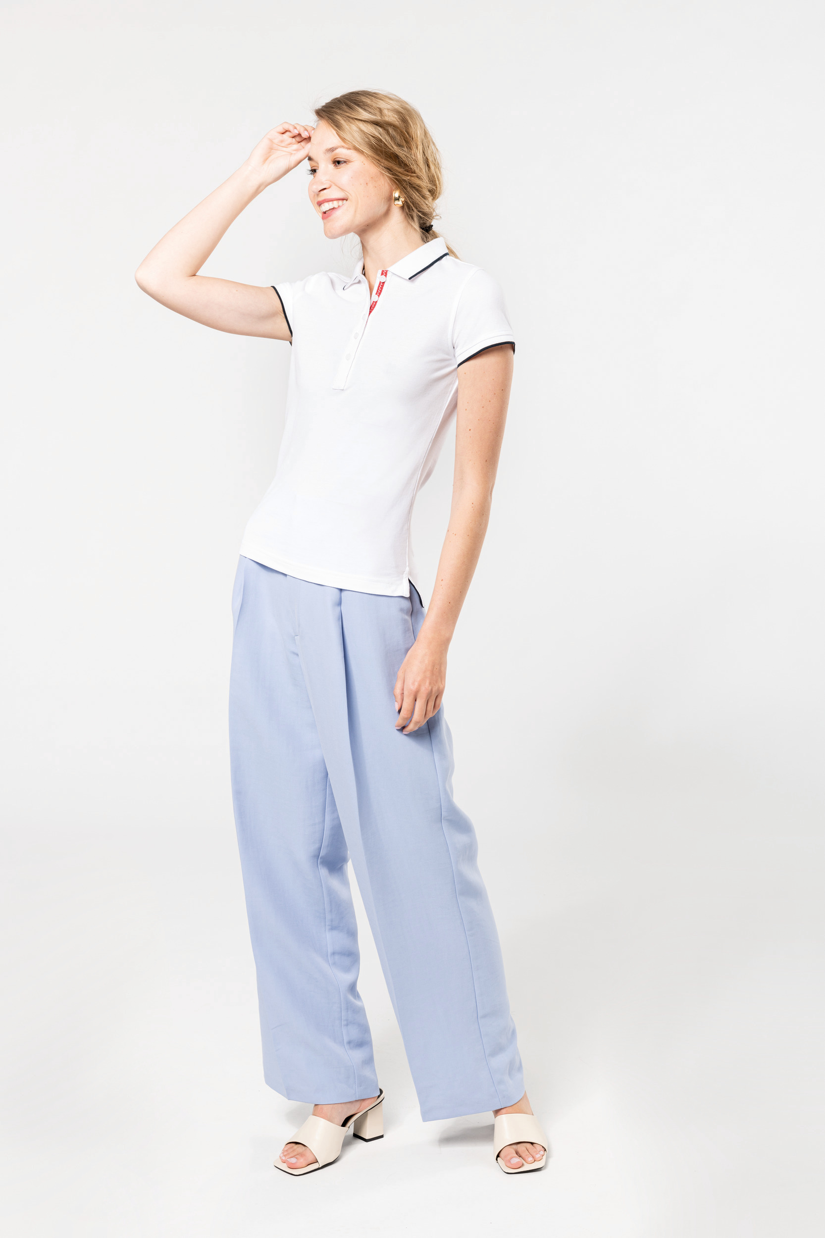 Mujer joven sonriente con polo blanco y pantalón ancho azul claro sobre fondo neutro