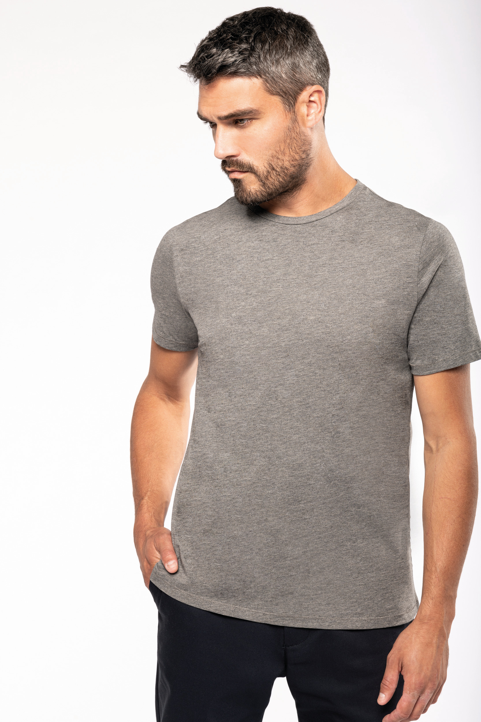 hombre con camiseta gris de manga corta y pantalones oscuros sobre fondo blanco