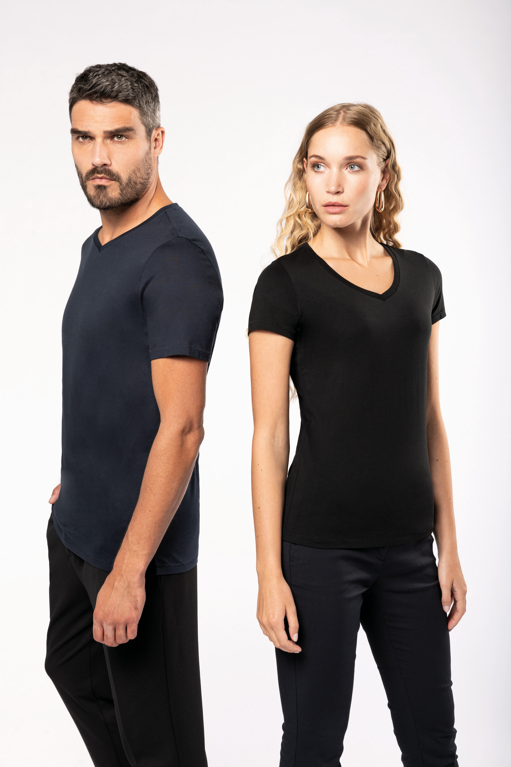 Pareja de modelos posando de lado con camisetas básicas de cuello en V sobre fondo blanco