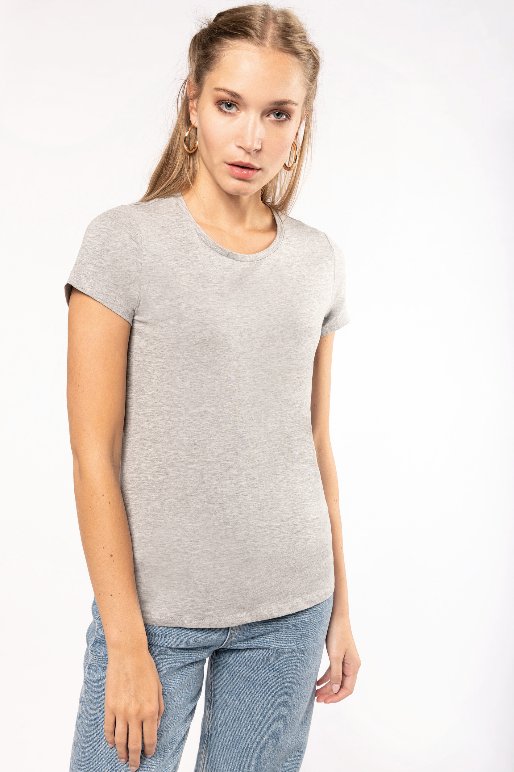 Mujer joven con camiseta gris de manga corta y vaqueros azules sobre fondo blanco