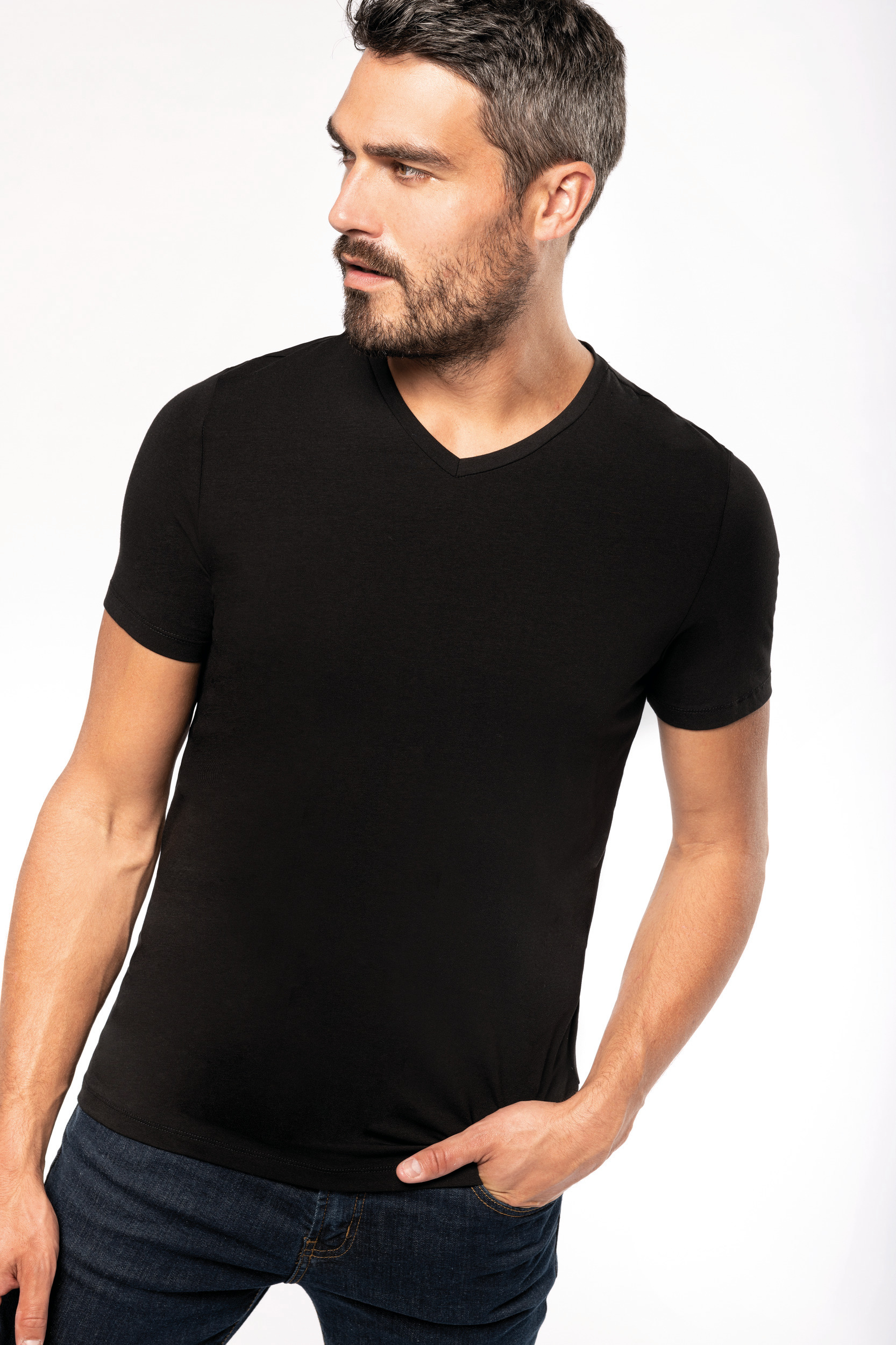 Hombre joven con camiseta negra de cuello pico y vaqueros sobre fondo blanco