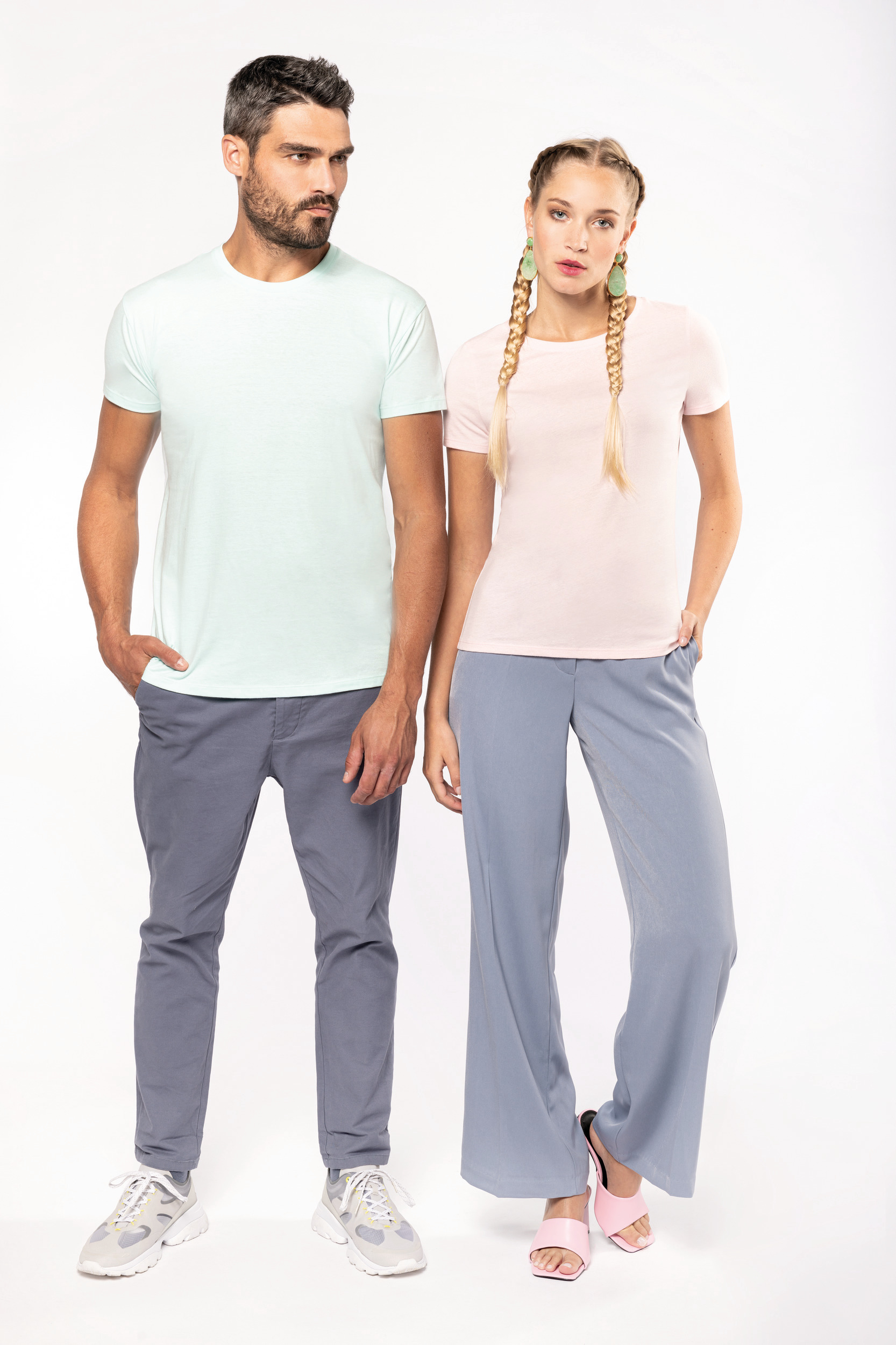 Pareja de modelos con camisetas de tonos pastel y pantalones grises sobre fondo blanco.