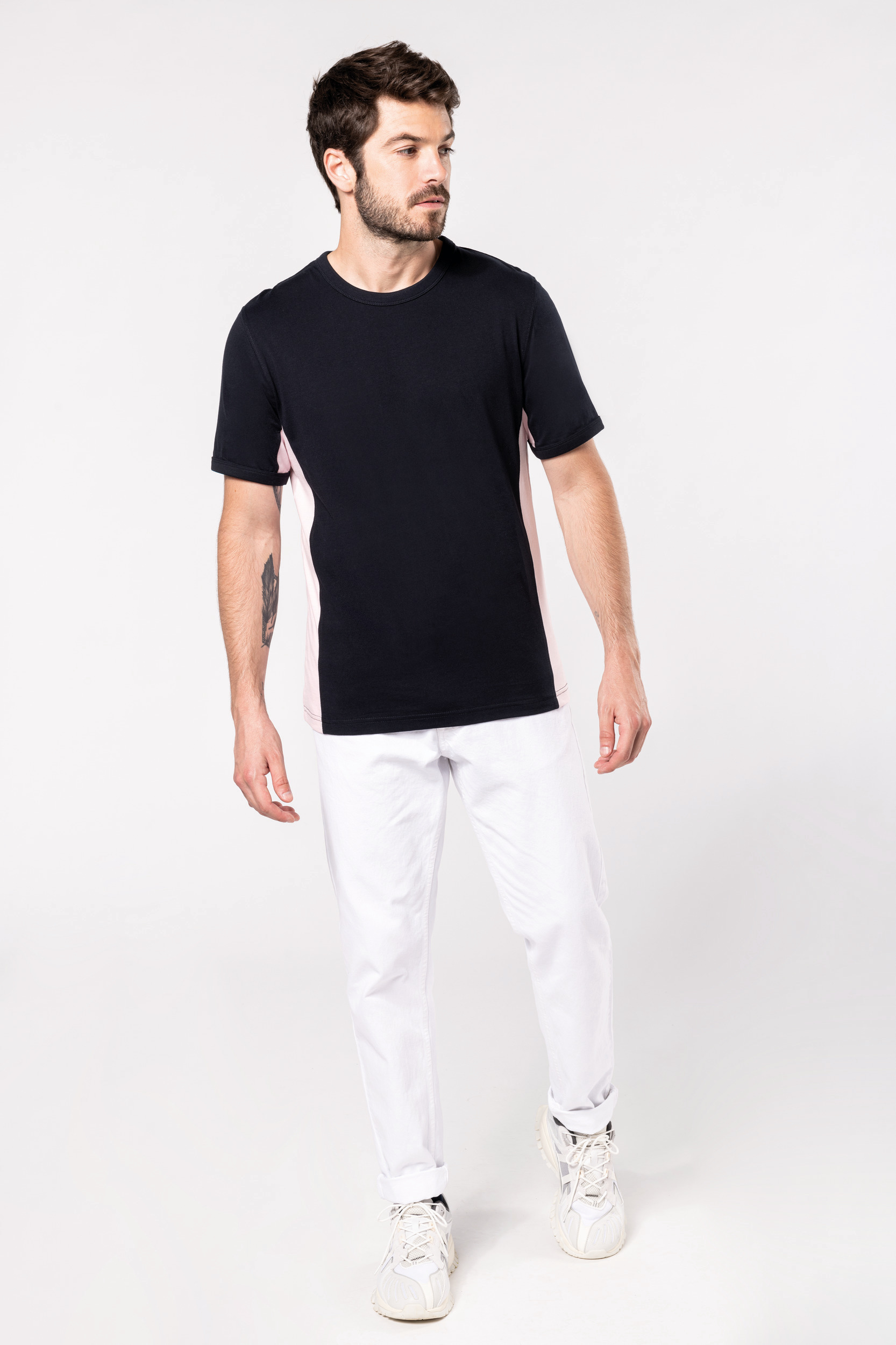 Hombre con camiseta negra de laterales rosas y pantalones blancos sobre fondo neutro