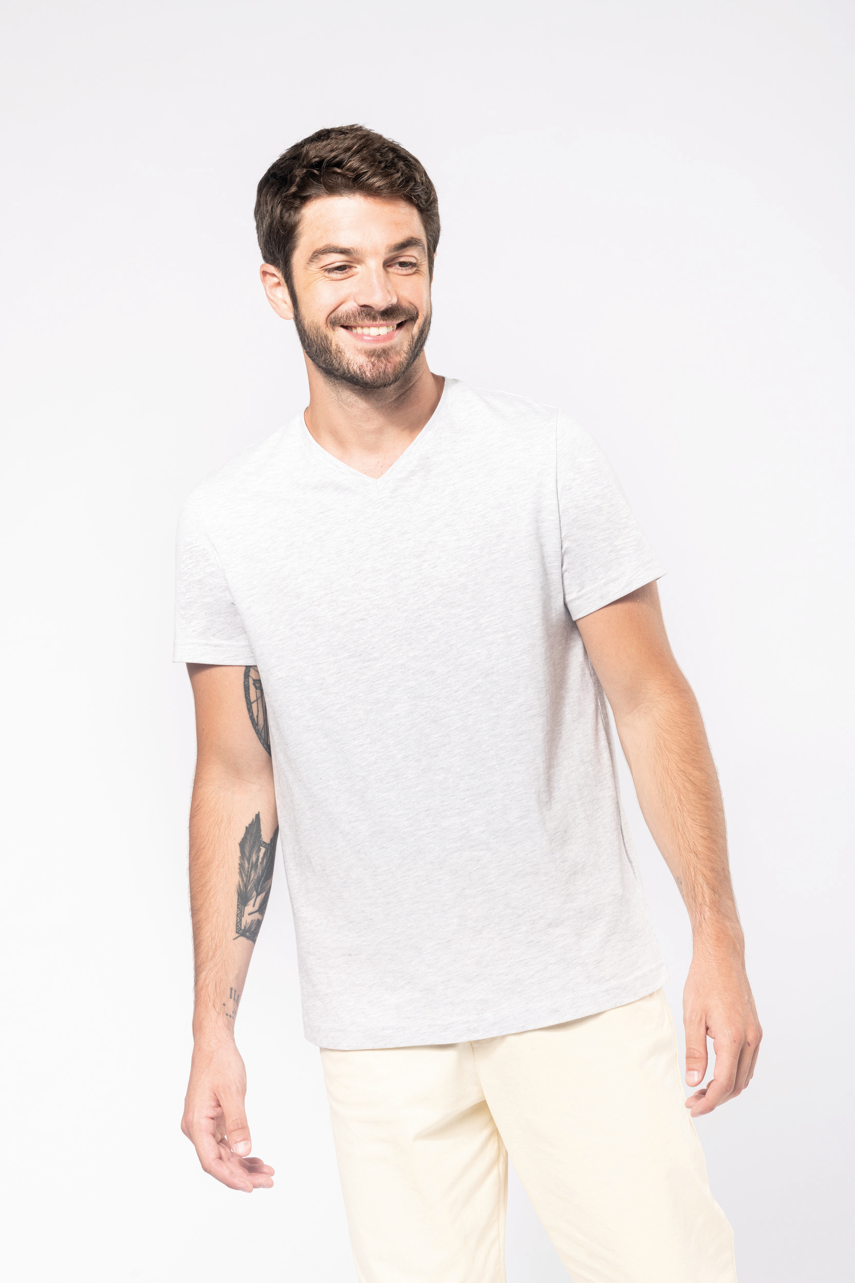 hombre joven sonriendo con camiseta gris clara y tatuaje en el antebrazo sobre fondo blanco