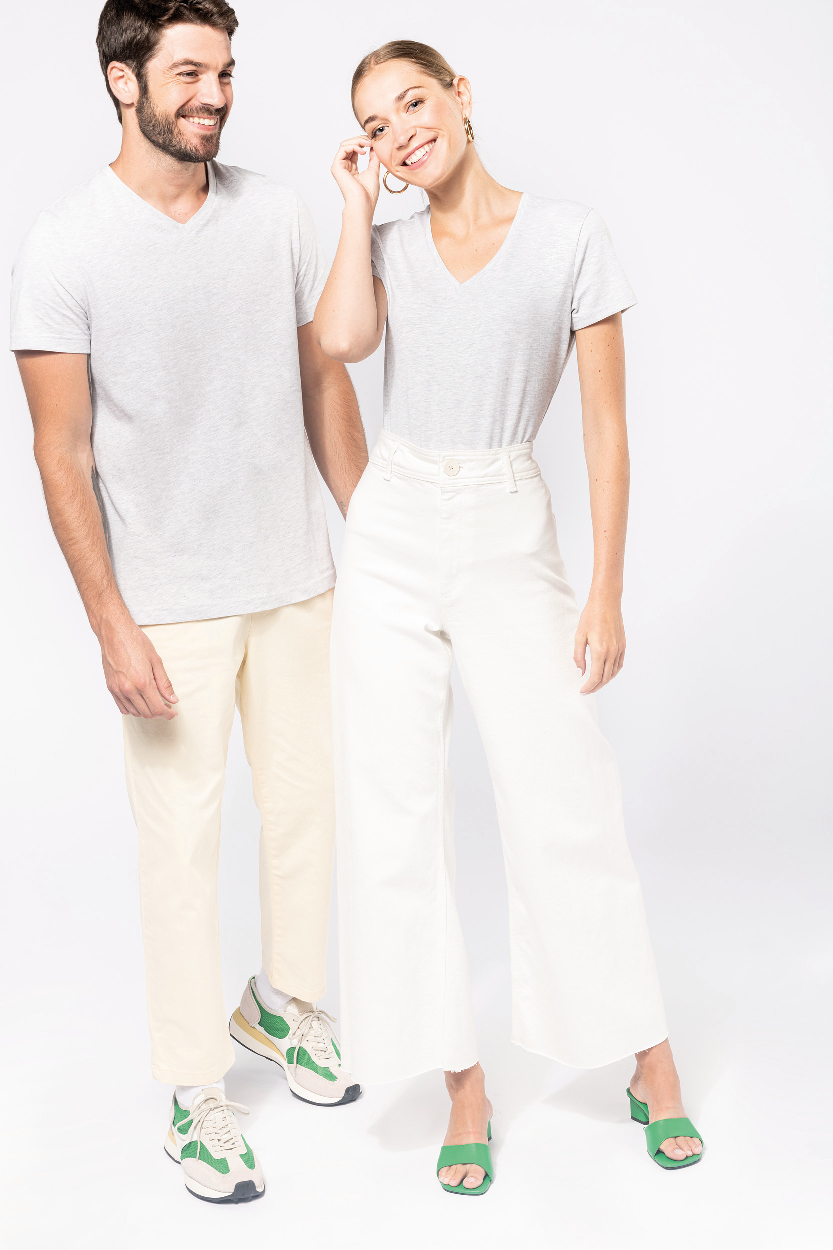Pareja de modelos con camisetas grises y pantalones claros posando sobre fondo blanco.