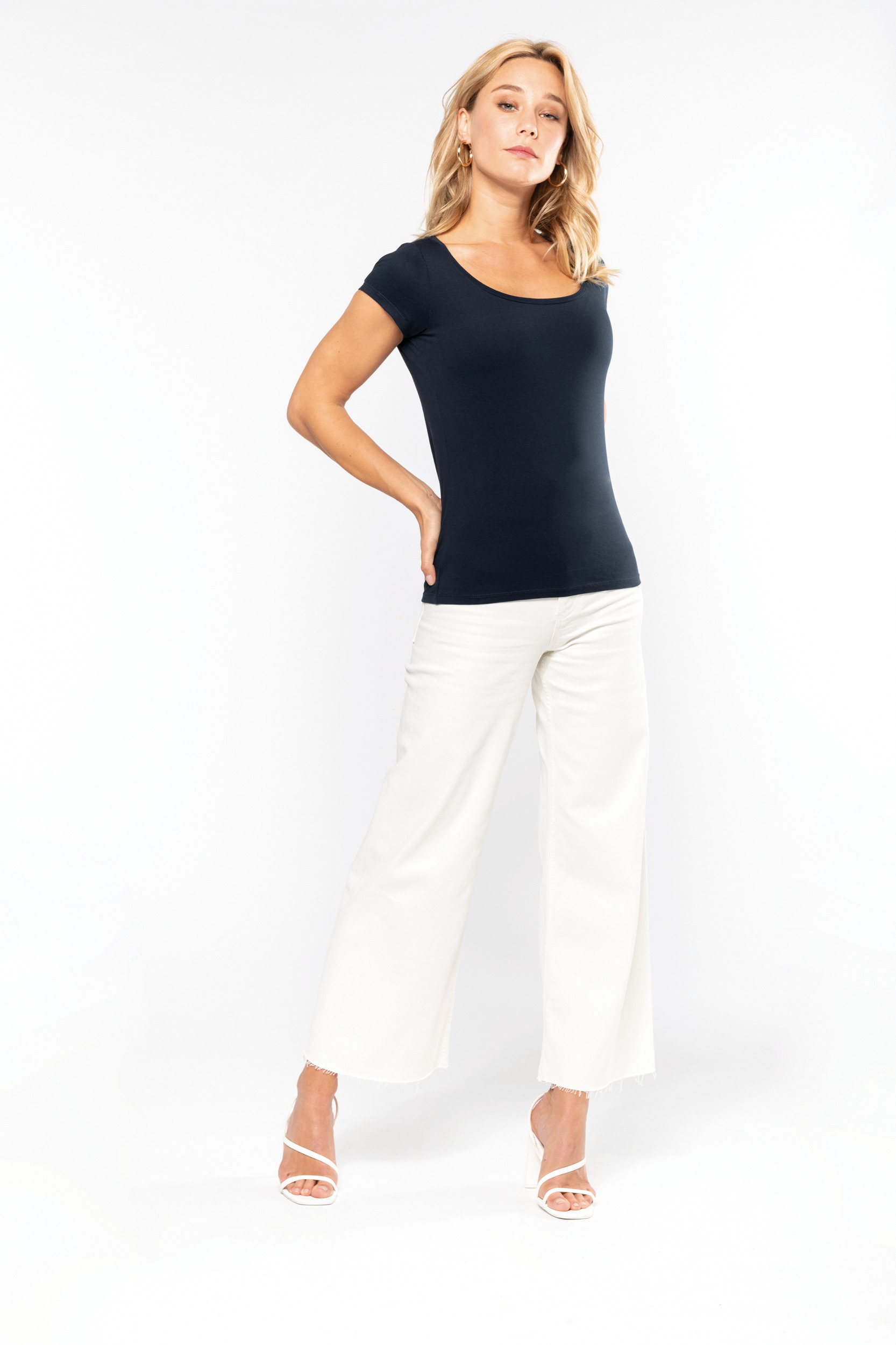 mujer de pie con camiseta azul marino de manga corta y pantalones blancos de pierna ancha sobre fondo blanco