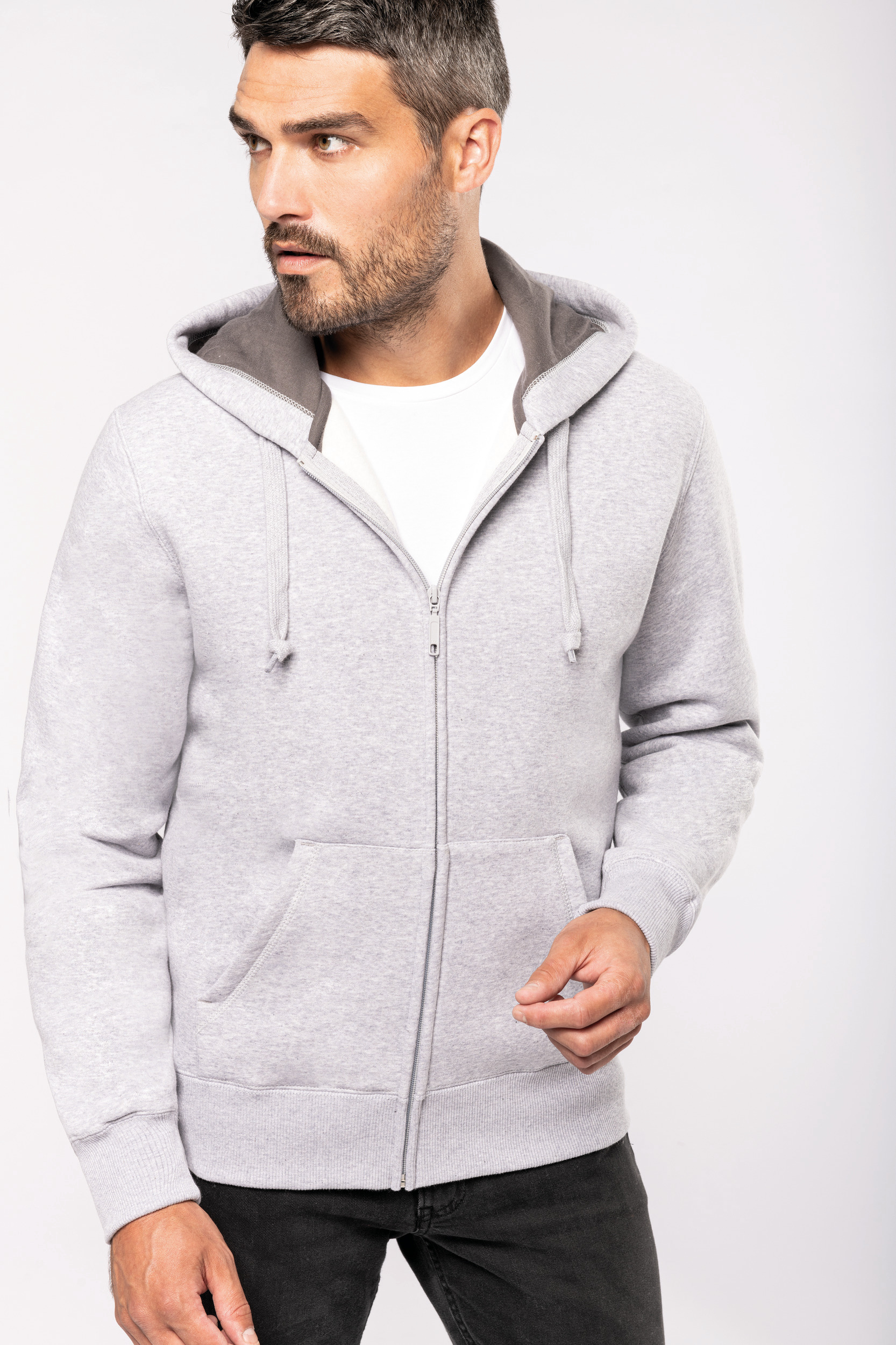 Hombre con sudadera gris con capucha y cremallera sobre camiseta blanca y pantalones oscuros