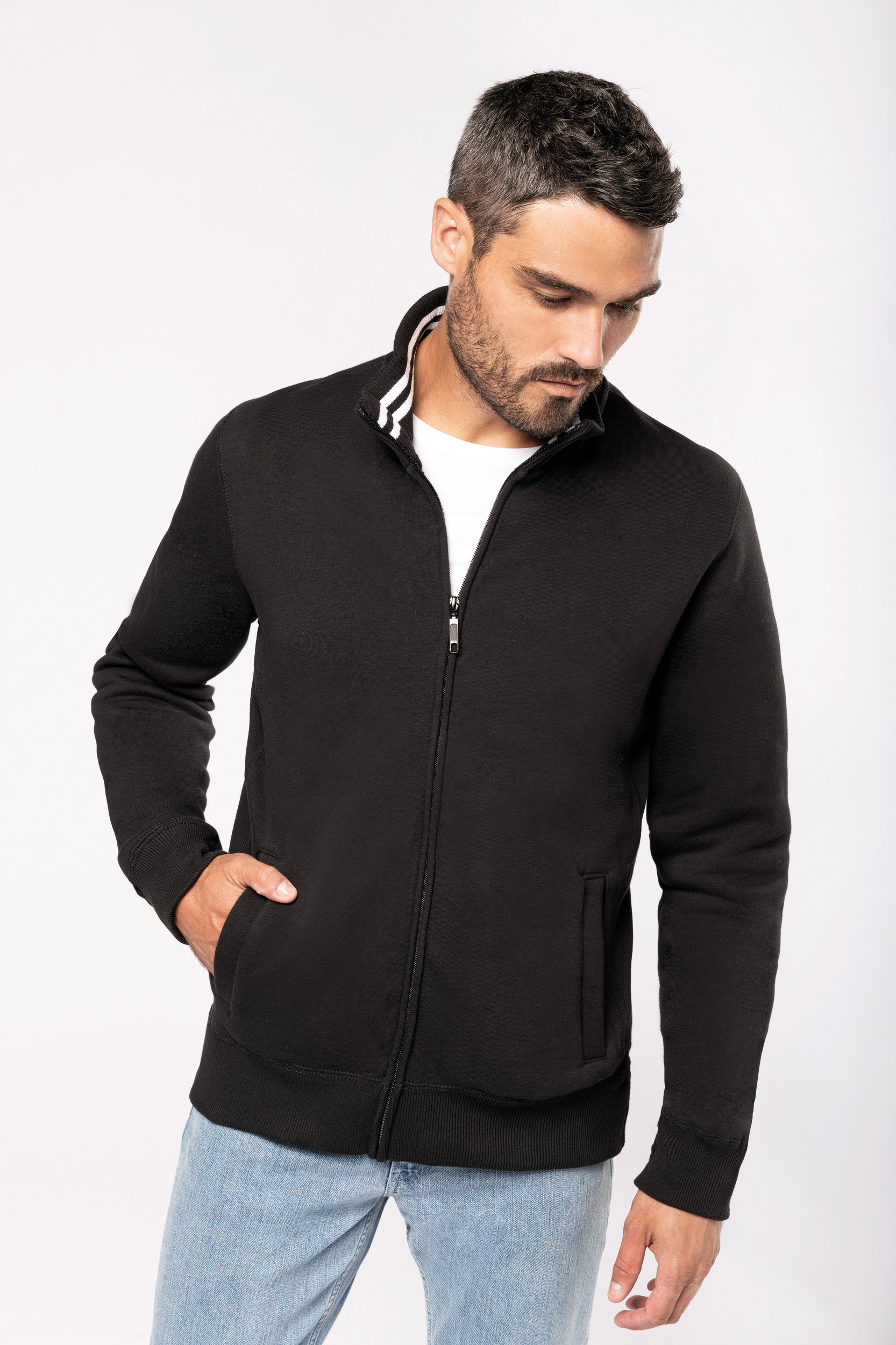 hombre con sudadera negra de cremallera y camiseta blanca en fondo neutro