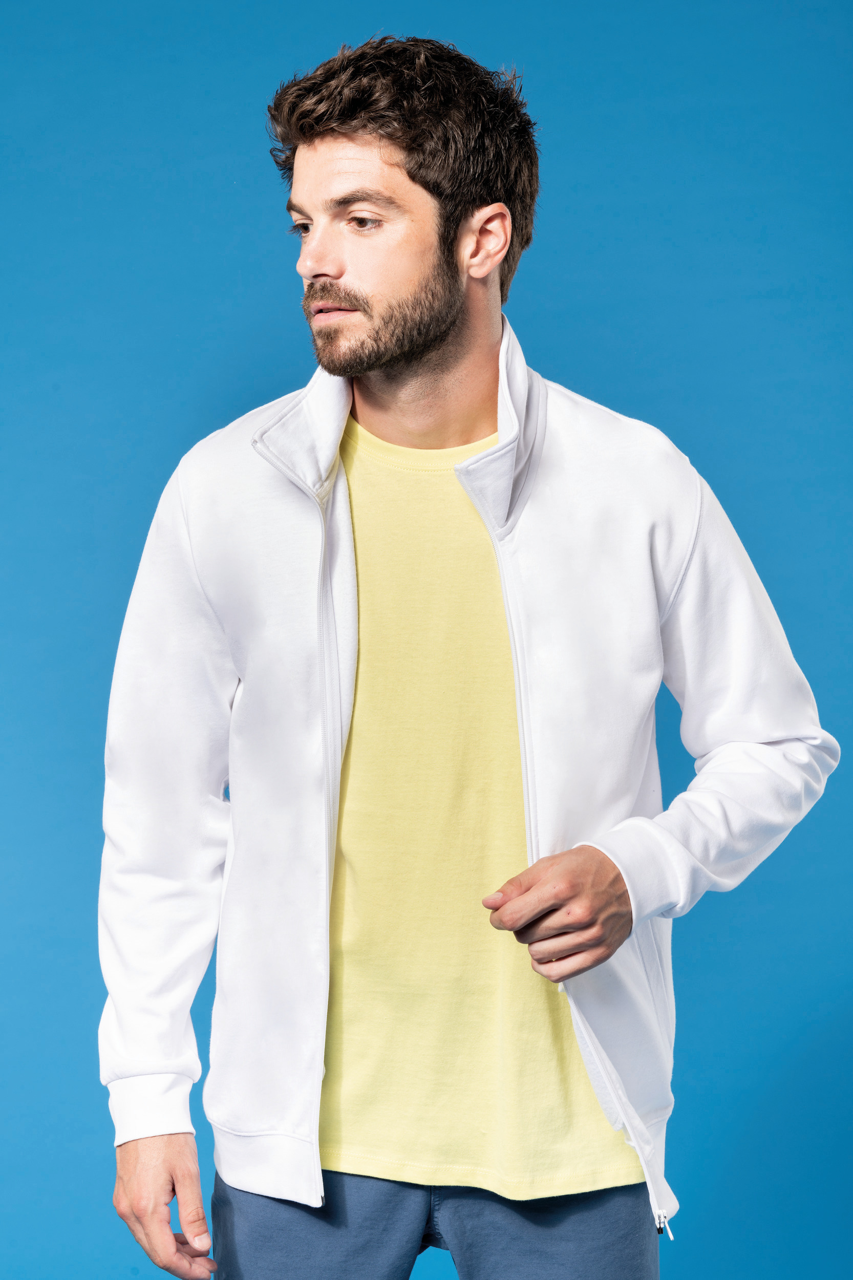 hombre con chaqueta deportiva blanca abierta sobre camiseta amarilla frente a fondo azul