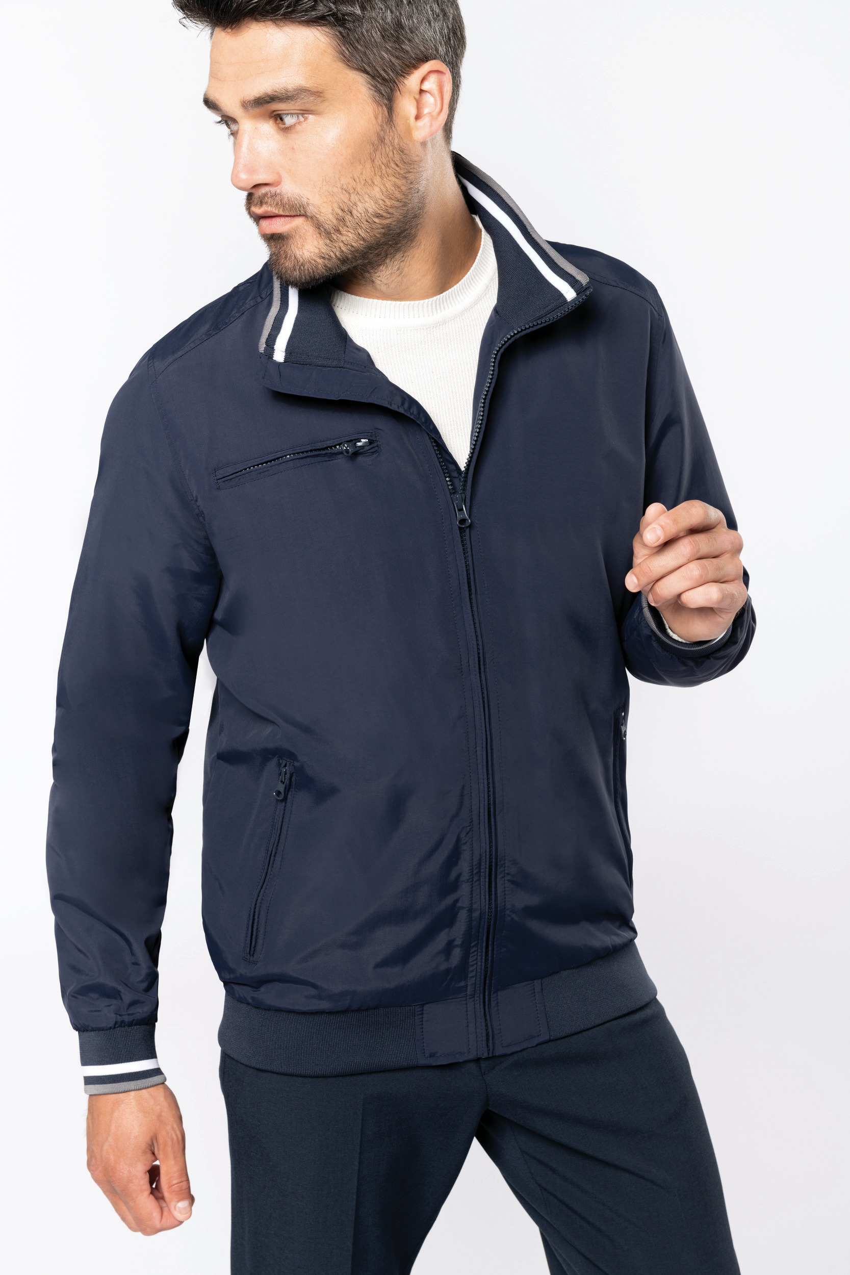 Hombre con cazadora bomber azul marino, suéter blanco y pantalones a juego.
