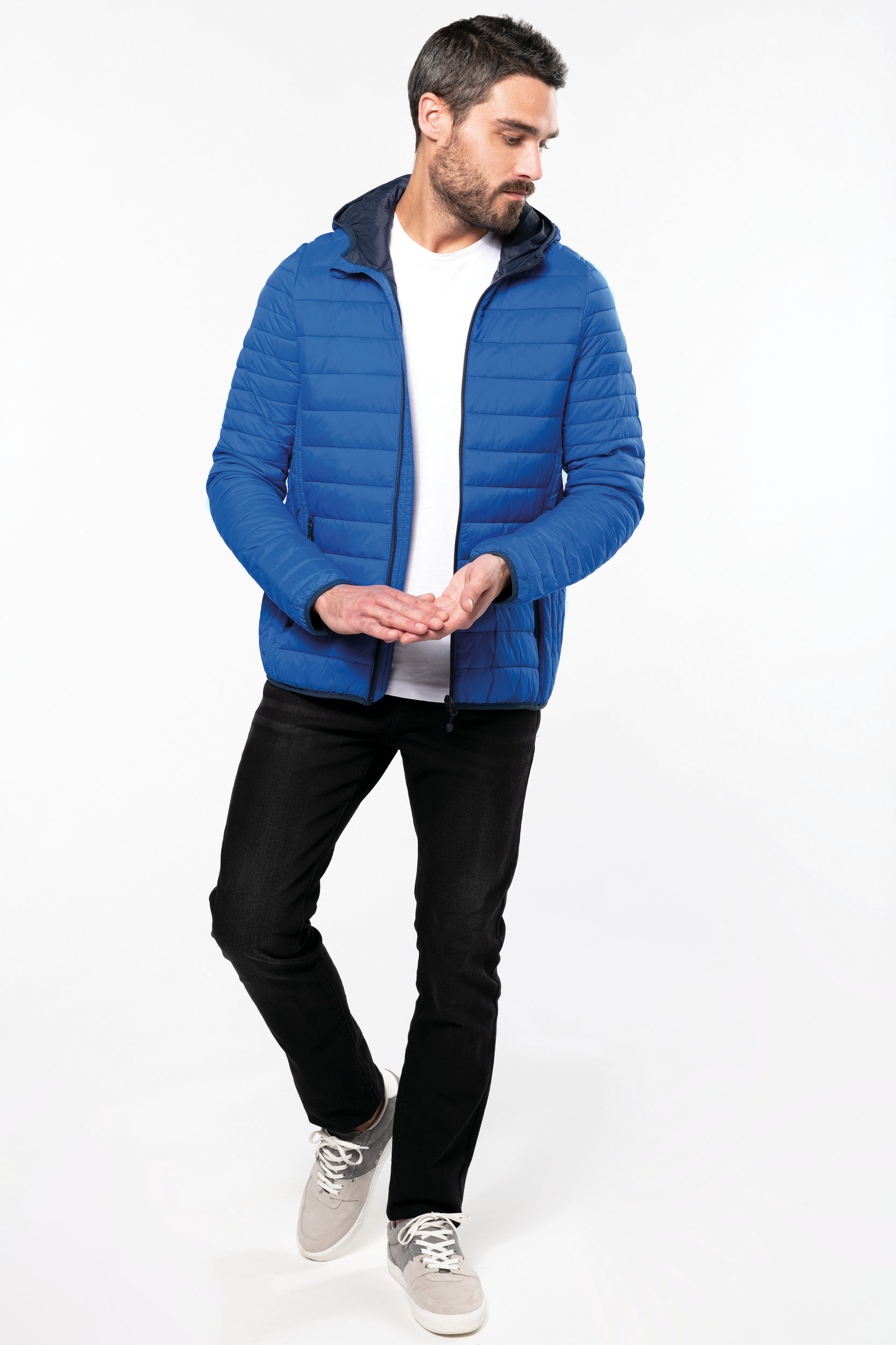 Hombre con chaqueta acolchada azul, camiseta blanca y vaqueros negros en estudio blanco.