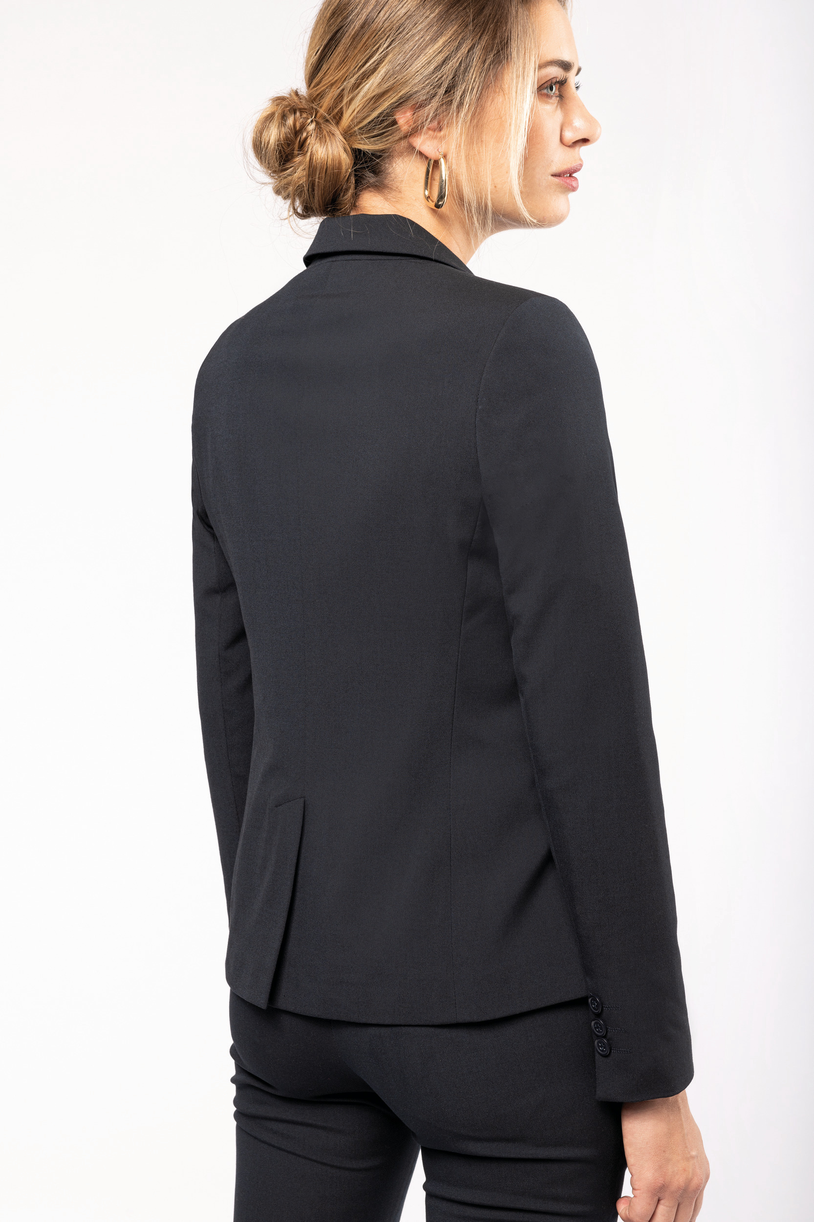 Mujer de perfil con traje sastre negro y cabello recogido de fondo blanco