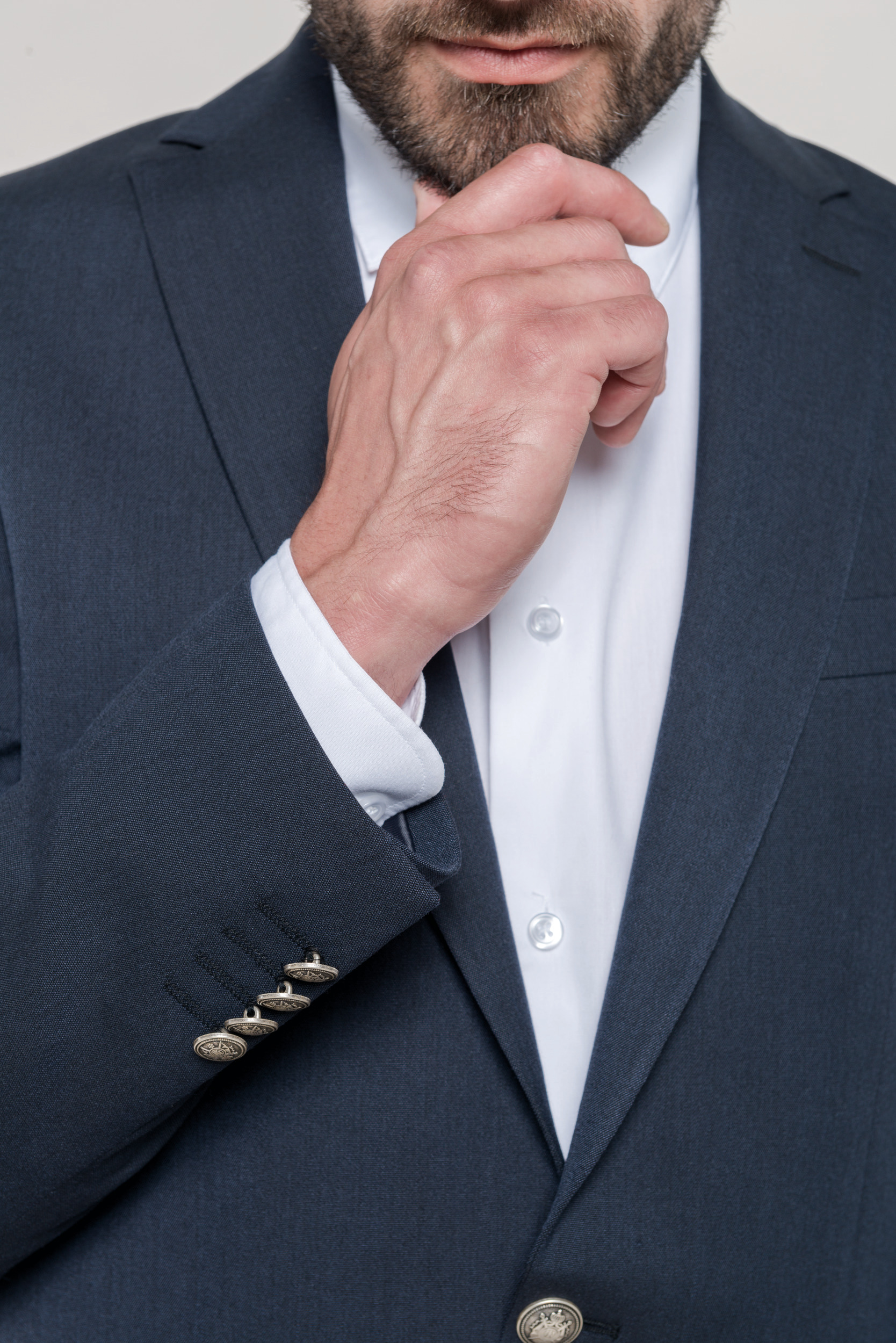 Hombre con traje azul marino y camisa blanca apoyando la barbilla en la mano en actitud pensativa