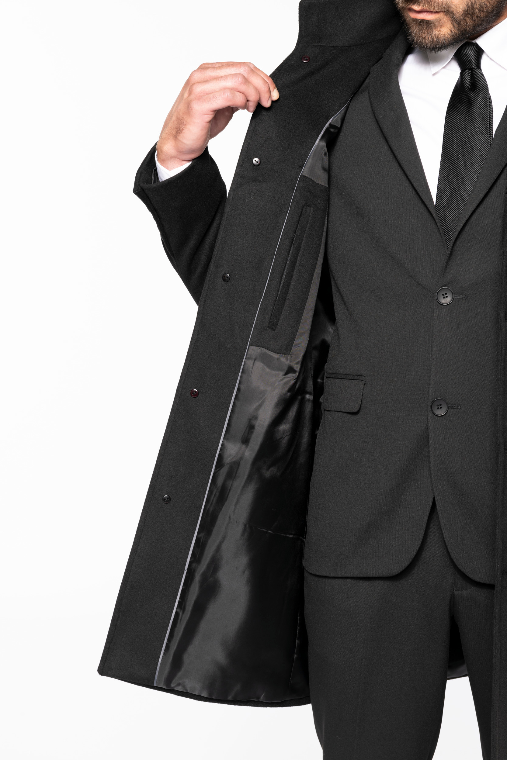 Hombre mostrando el forro interior de un abrigo negro sobre un traje y corbata.