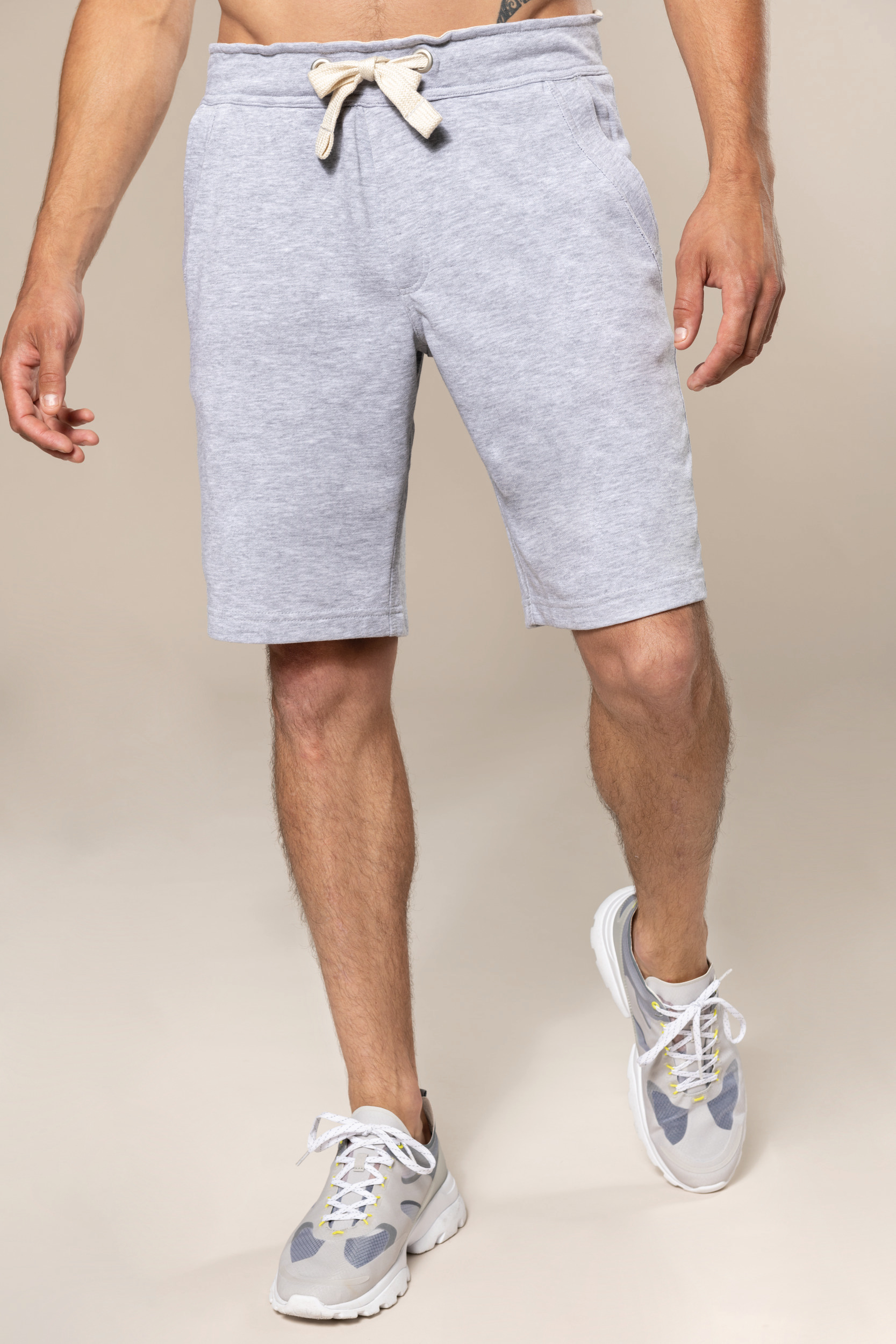 Hombre de pie con bermudas de sudadera grises y zapatillas deportivas grises.
