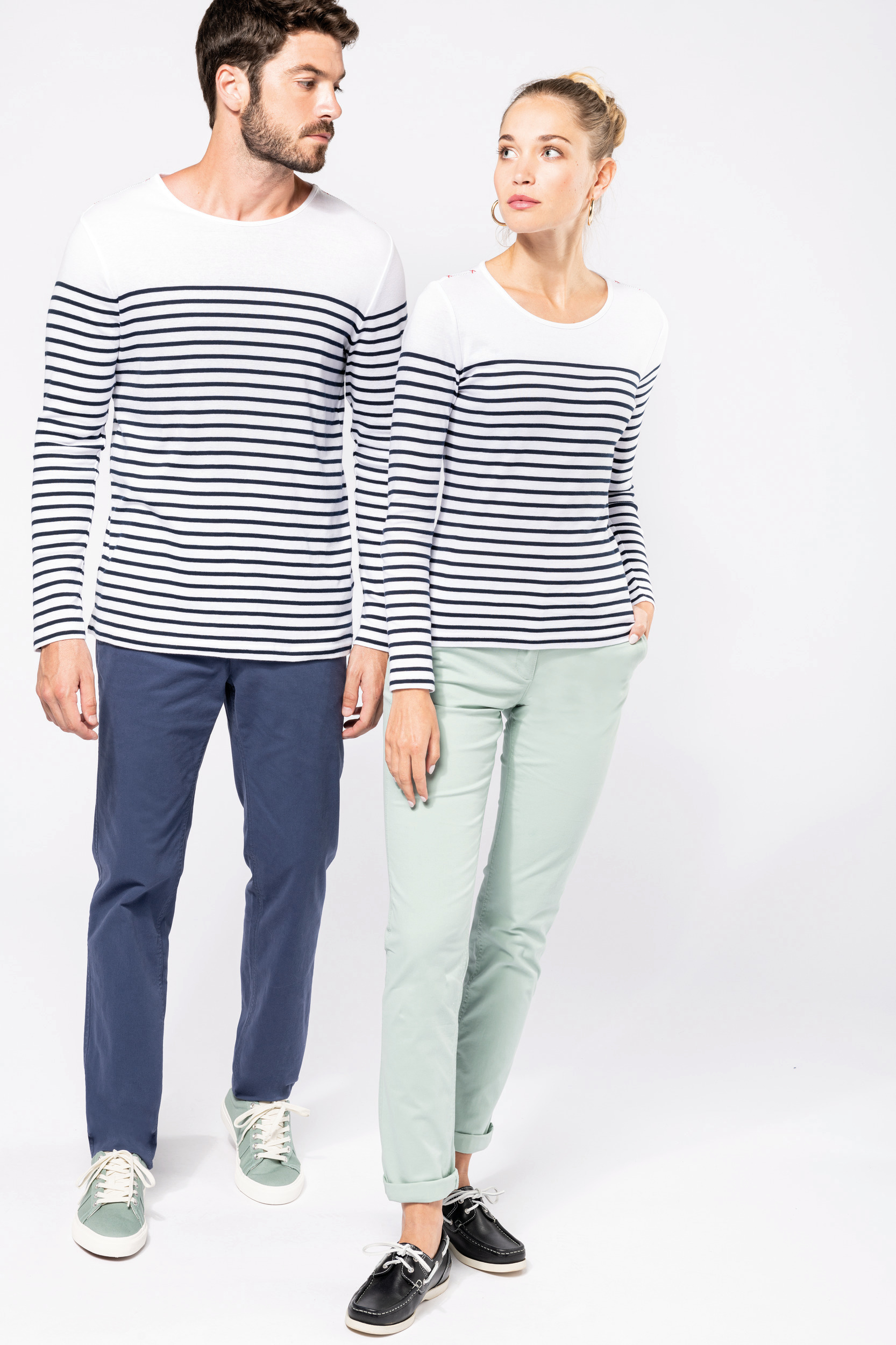 Hombre y mujer de pie con camiseta de rayas marineras y pantalones chinos en fondo blanco