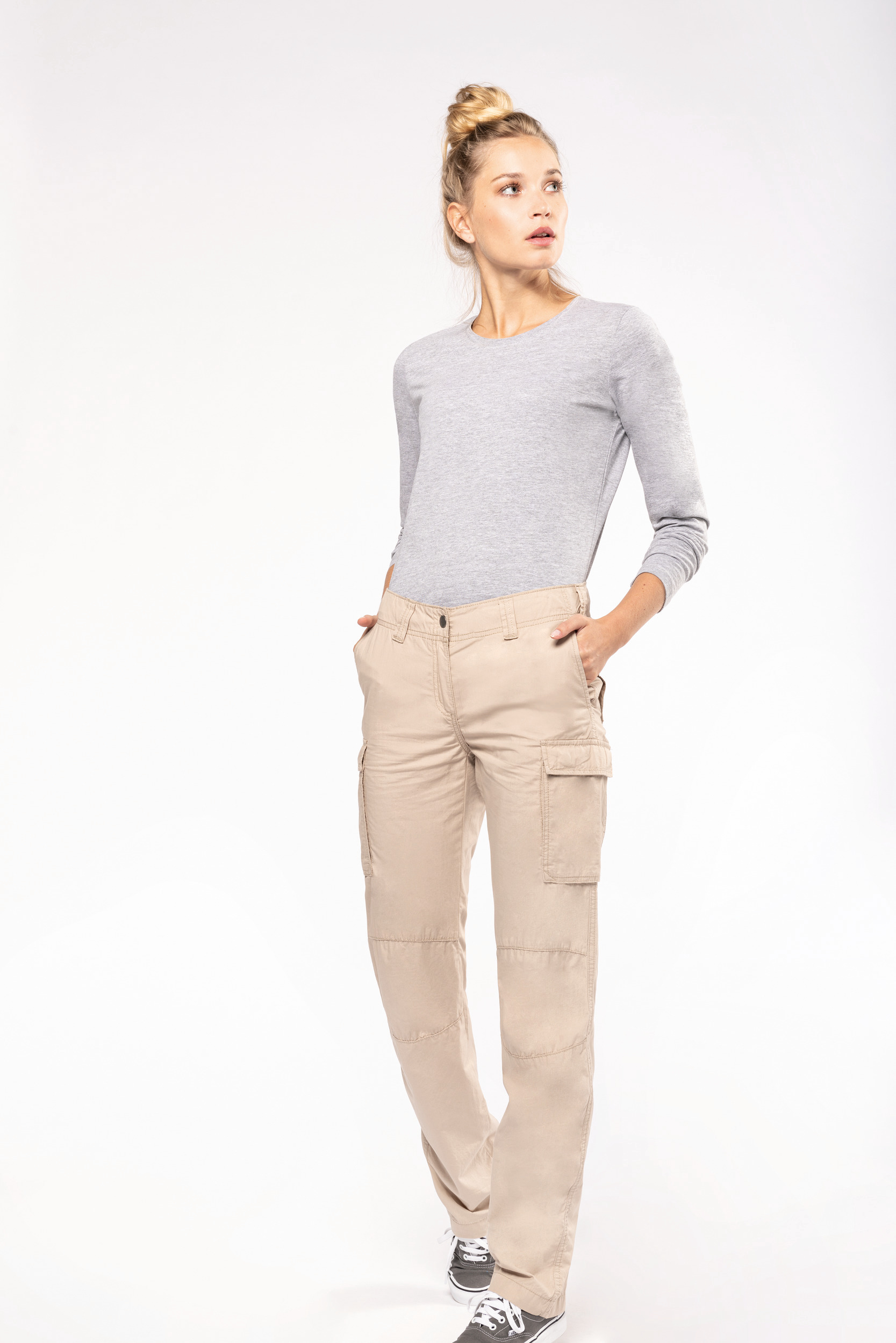 Mujer con camiseta gris de manga larga y pantalones cargo beige posando sobre fondo blanco