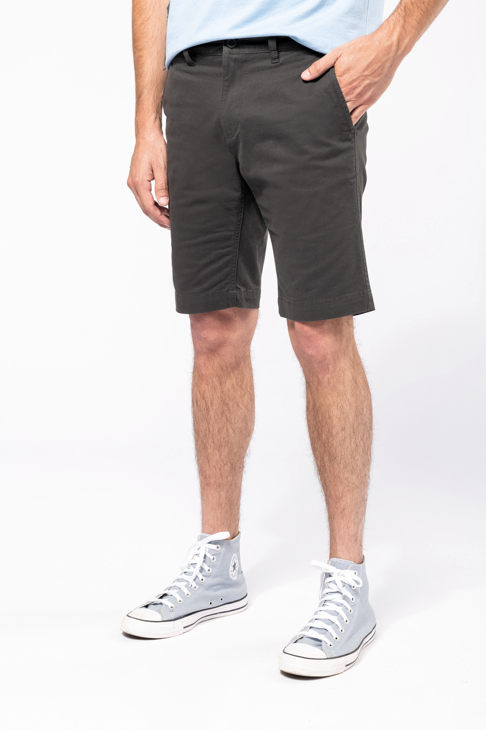 Primer plano de un hombre de pie con bermudas gris oscuro y zapatillas altas celeste sobre fondo blanco.
