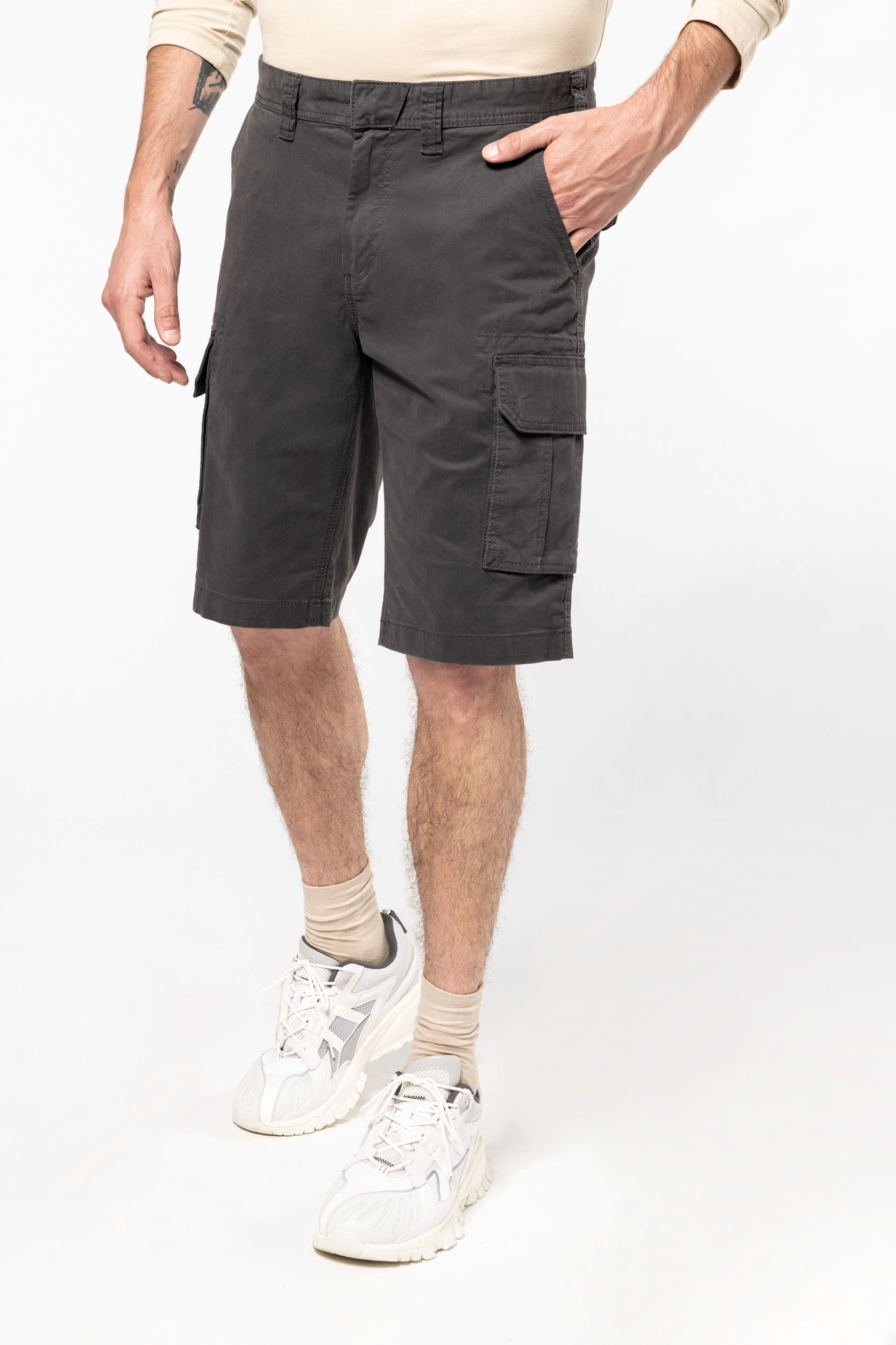 Hombre de pie con bermudas cargo grises, calcetines beige y zapatillas blancas.