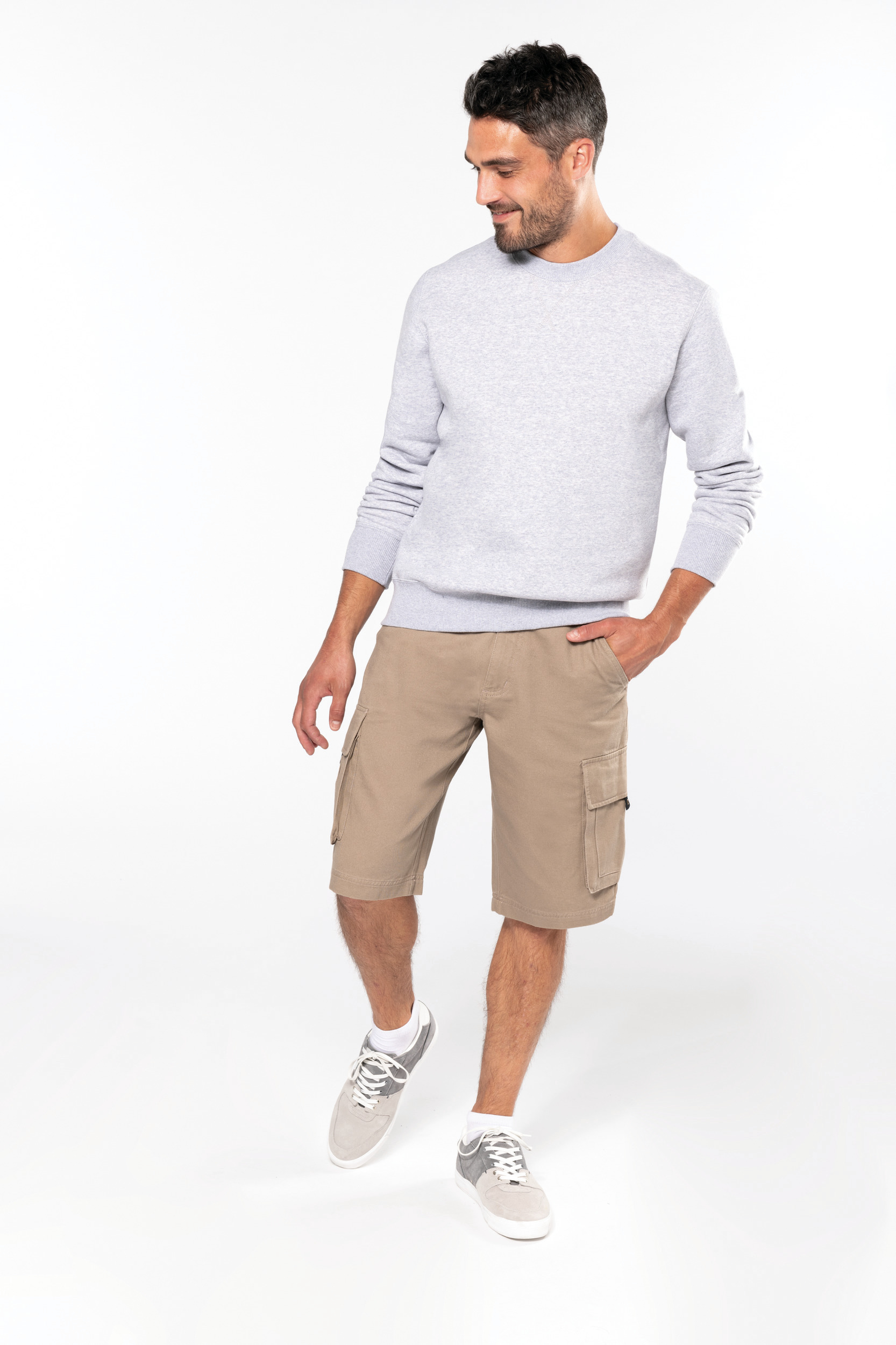 Hombre con sudadera gris, bermudas beige con bolsillos laterales y zapatillas deportivas sobre fondo blanco