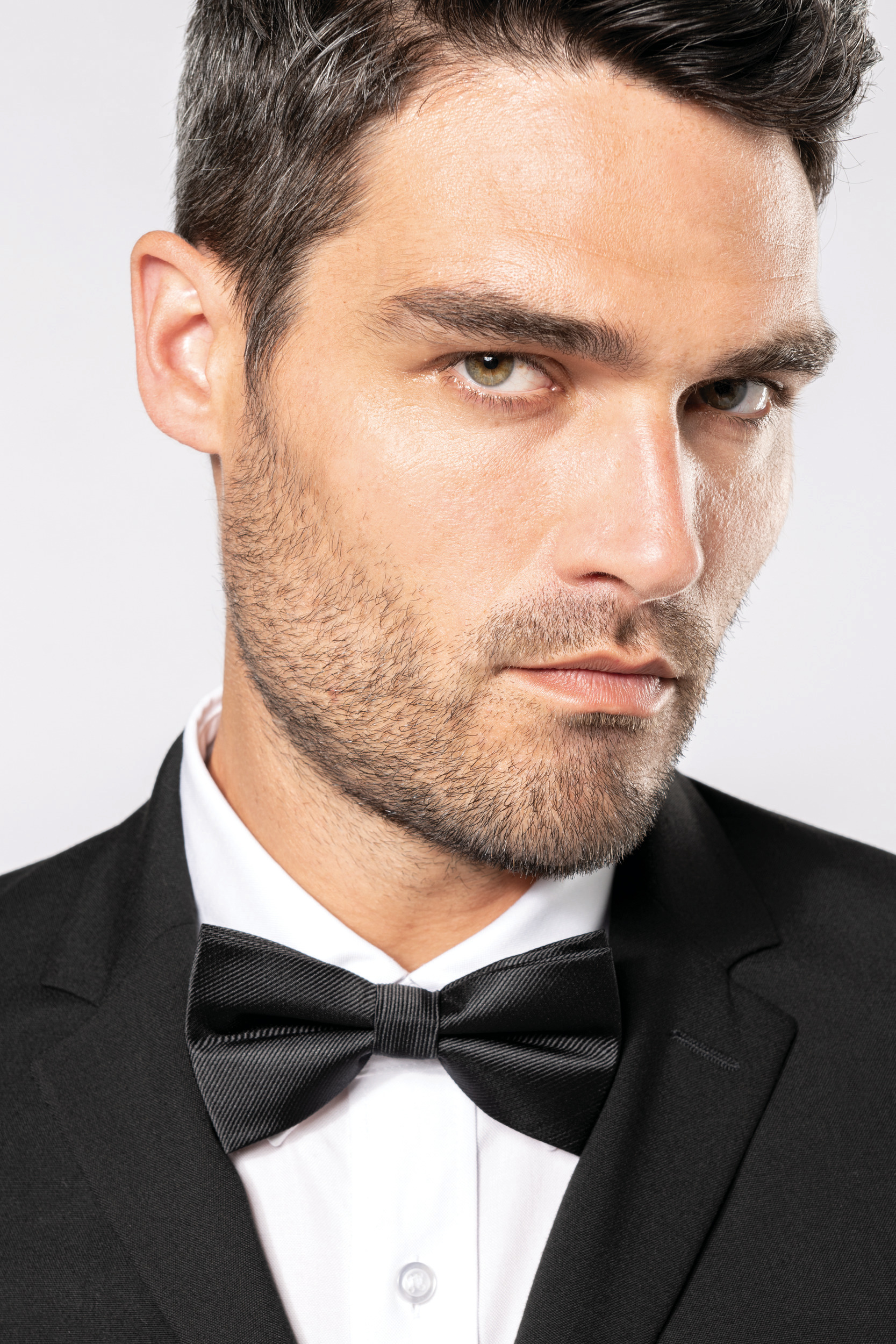 hombre con esmoquin negro y pajarita mirando de frente con expresión seria