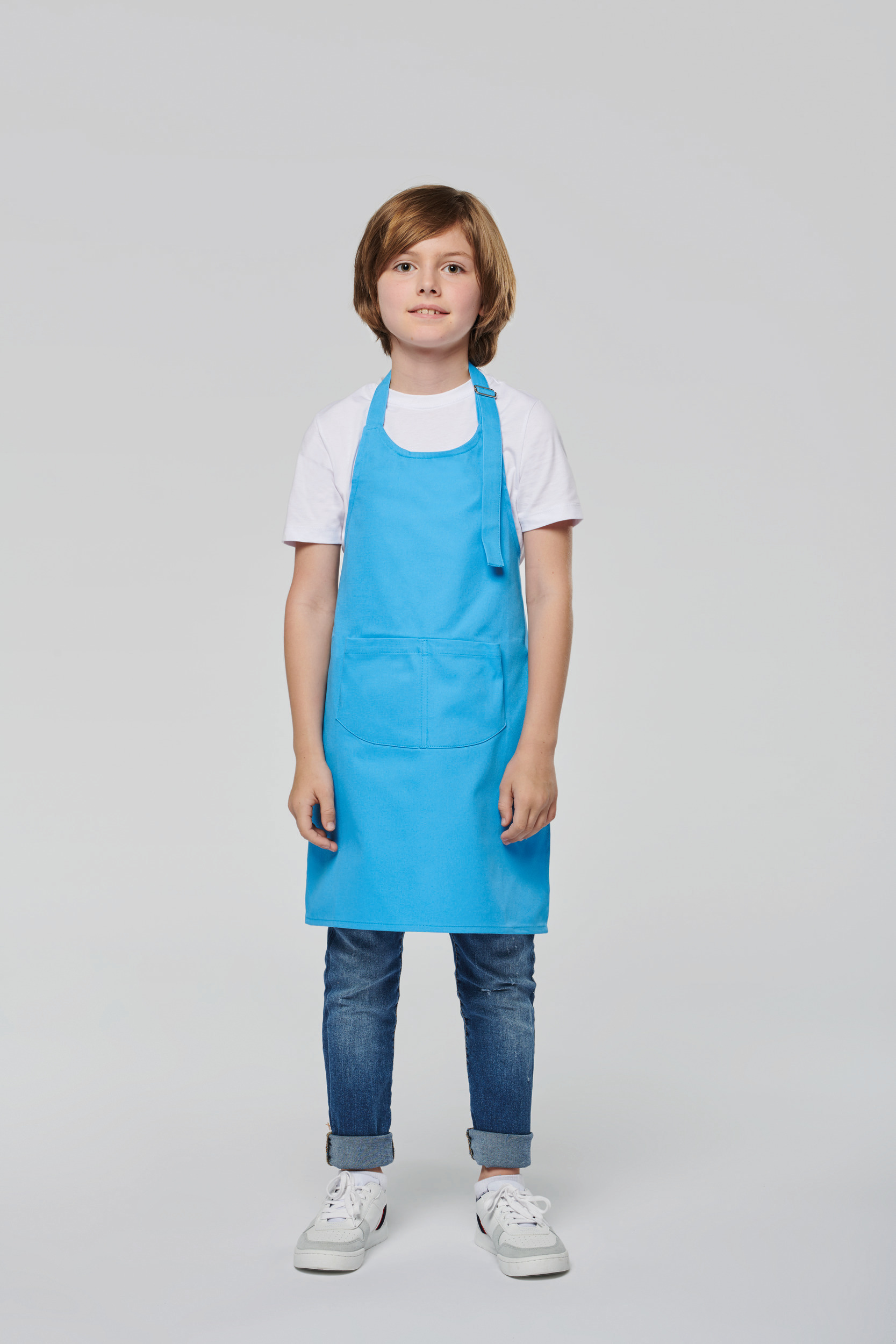 Niño con delantal azul y vaqueros sobre fondo neutro.