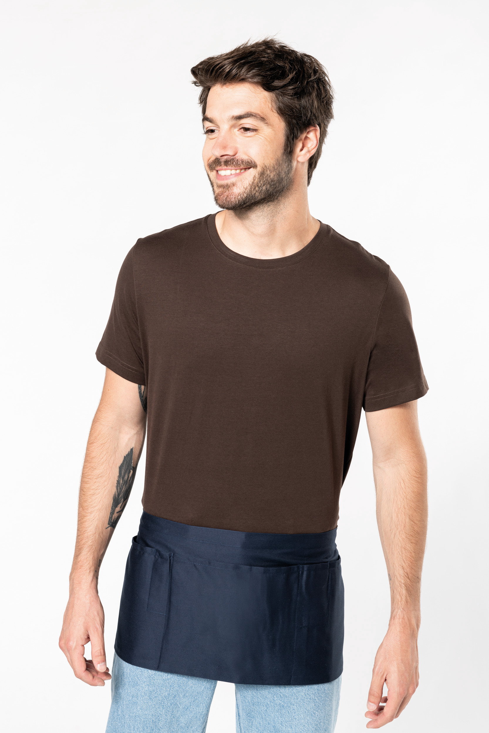 Hombre con camiseta marrón y delantal corto azul marino atado a la cintura.