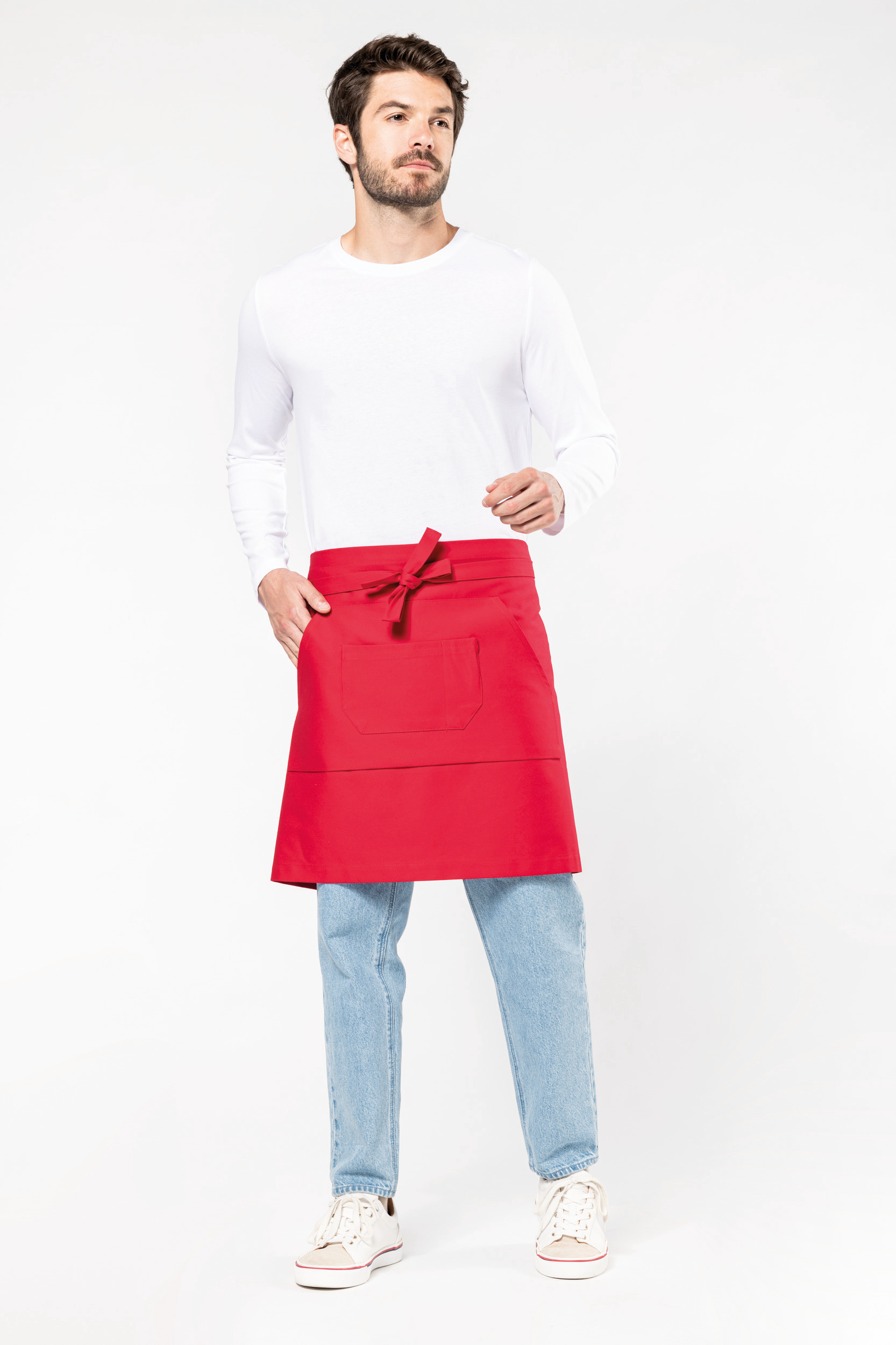 Hombre de pie con delantal rojo de cintura, camiseta blanca y vaqueros sobre fondo blanco