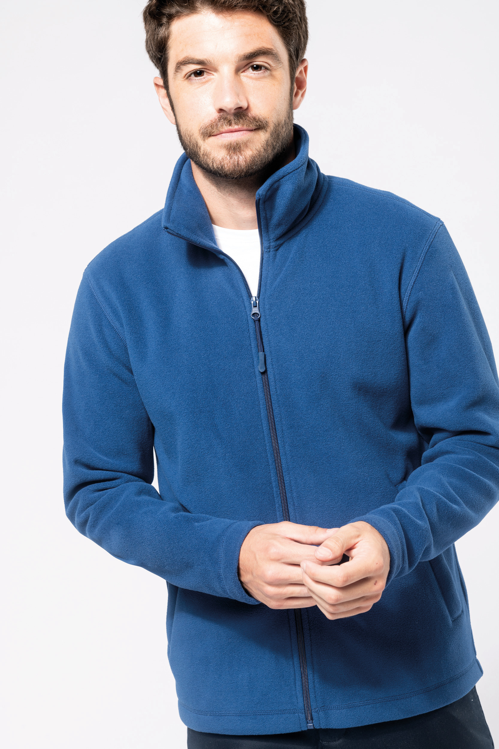 Hombre joven con chaqueta polar azul de manga larga y cremallera sobre fondo blanco