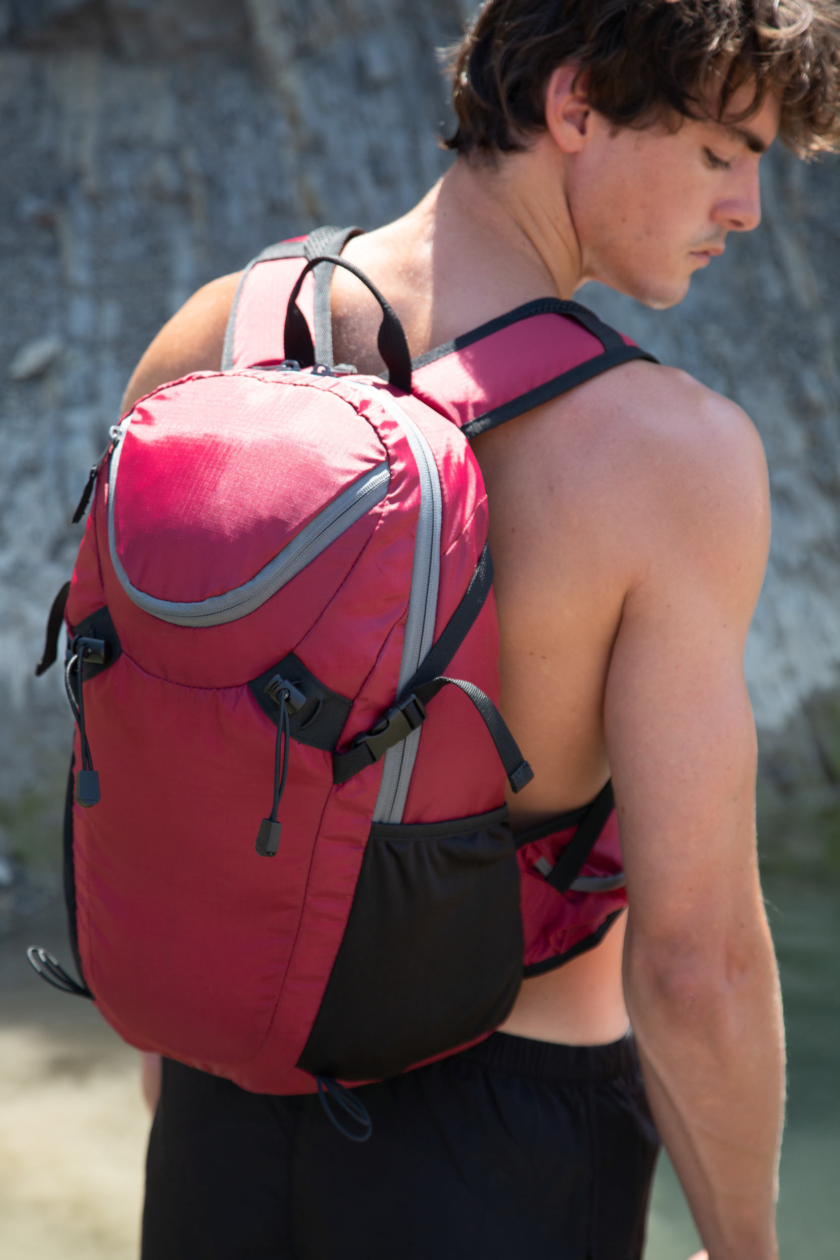 hombre joven con mochila de senderismo roja junto a pared rocosa