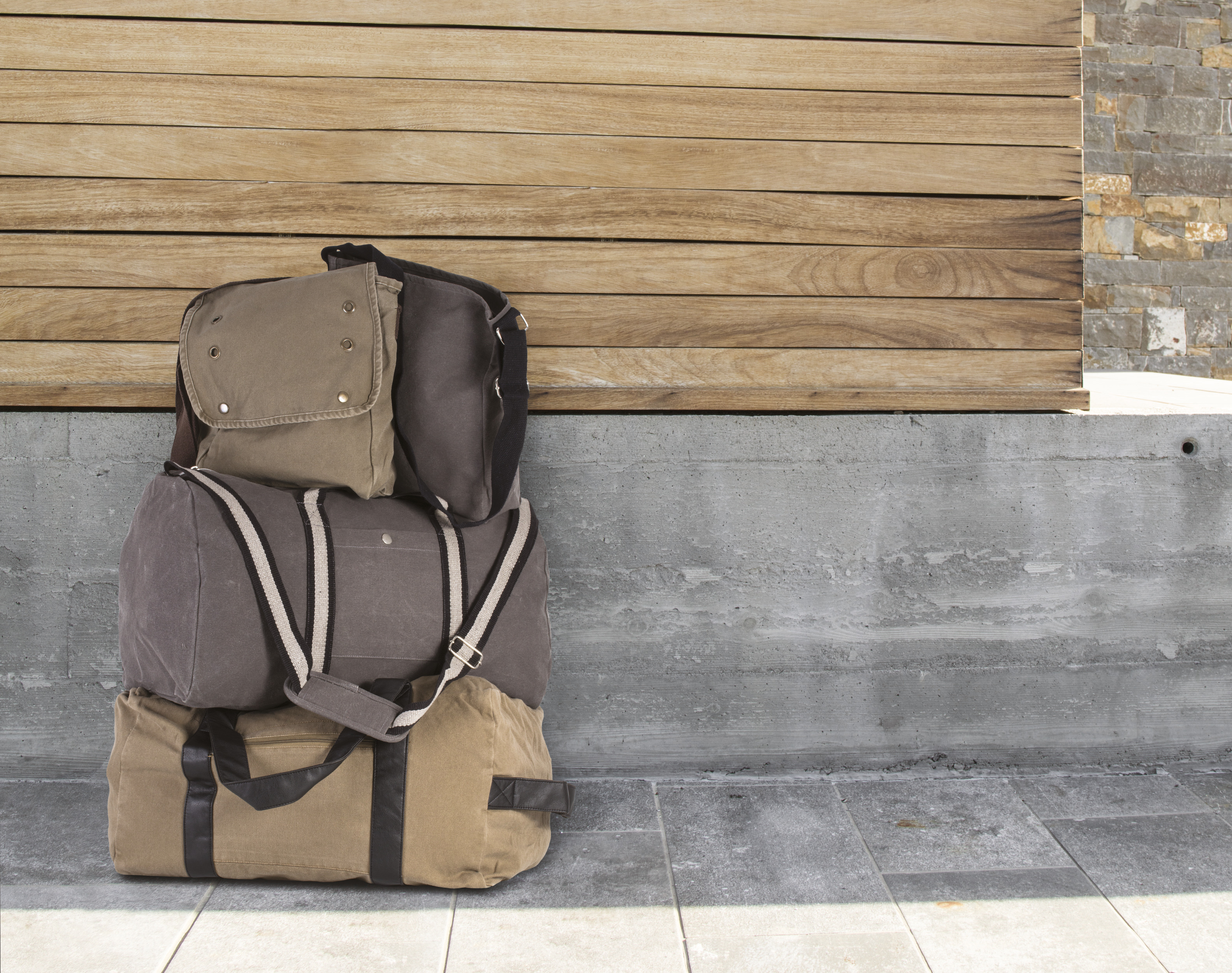 tres bolsas de lona de viaje apiladas frente a un muro de hormigón y paneles de madera