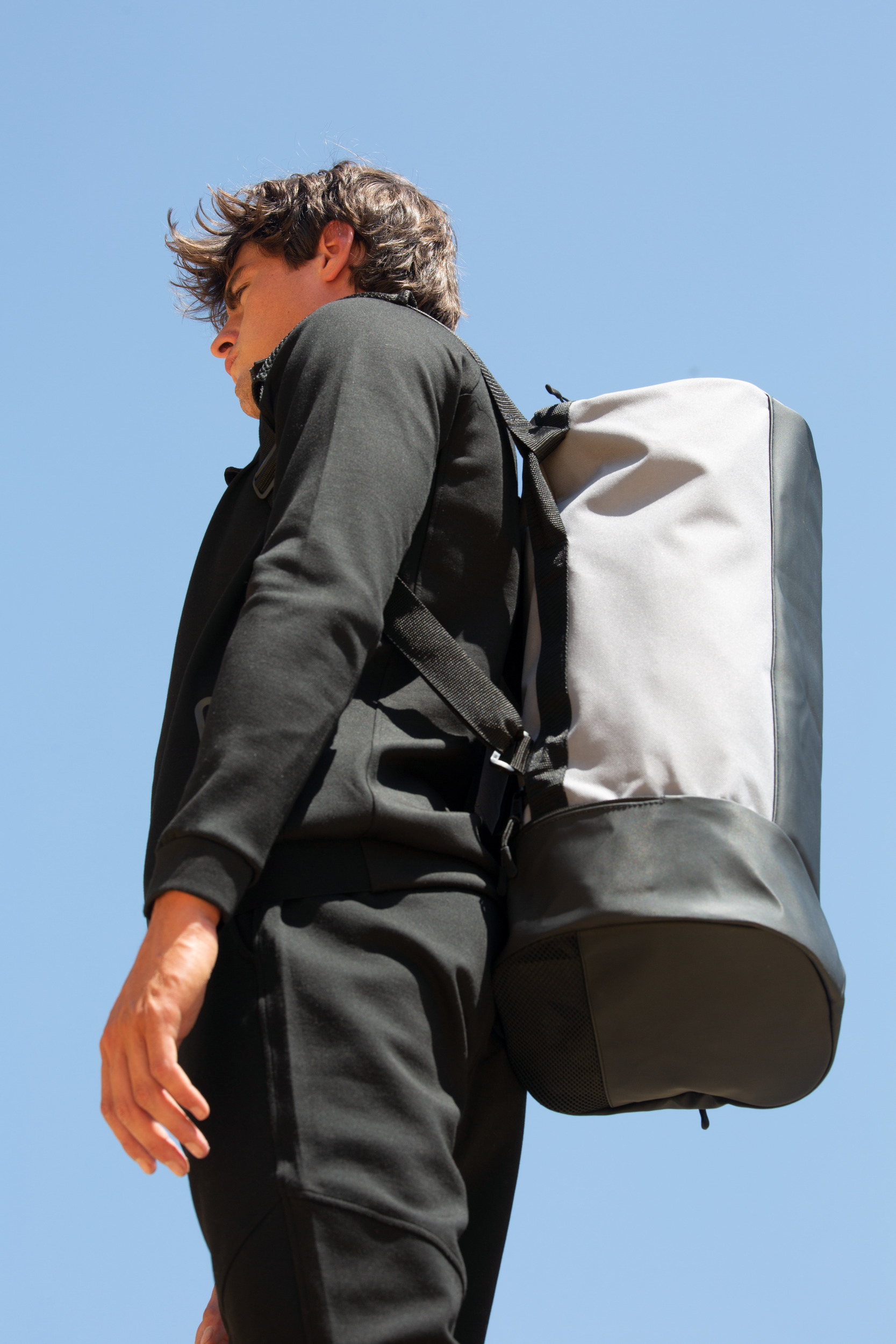 Hombre con sudadera negra y mochila gris frente a un cielo despejado