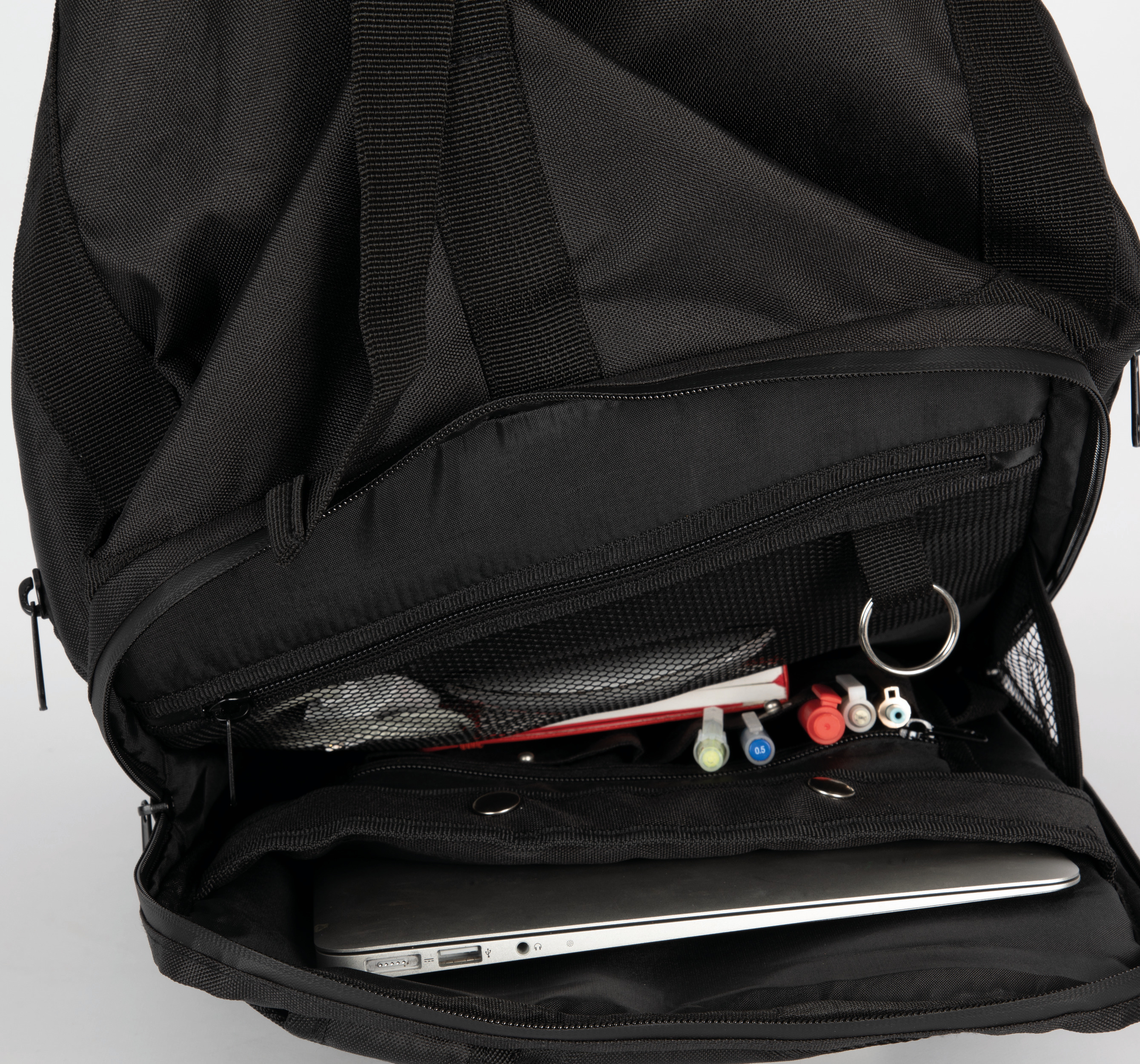 Mochila negra abierta con portátil, bloc de notas y bolígrafos organizados en sus compartimentos internos