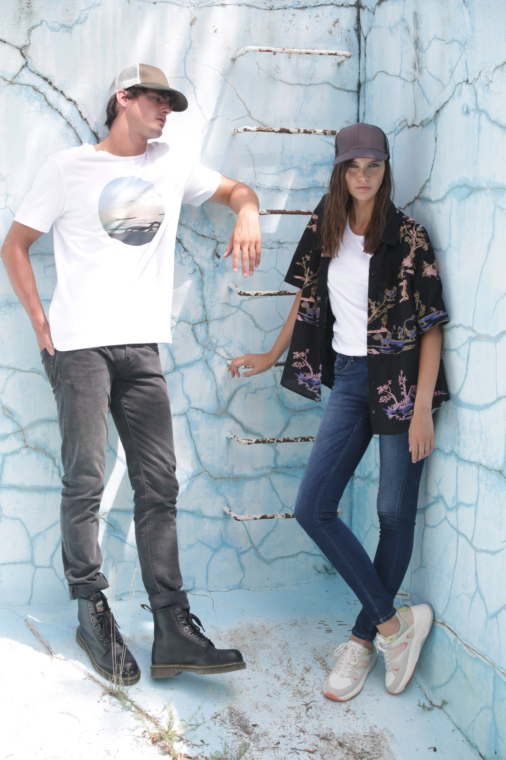 Jóvenes con gorras y ropa casual apoyados en una pared azul agrietada en una sesión de moda urbana.