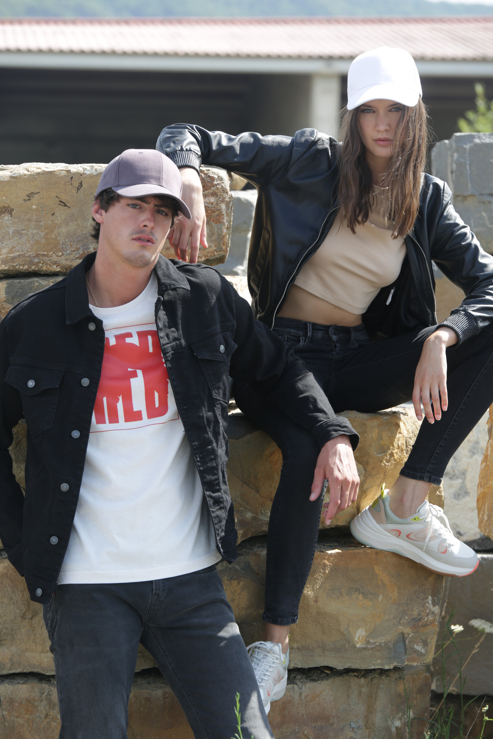 hombre y mujer con gorras y chaquetas informales sentados sobre grandes rocas al aire libre