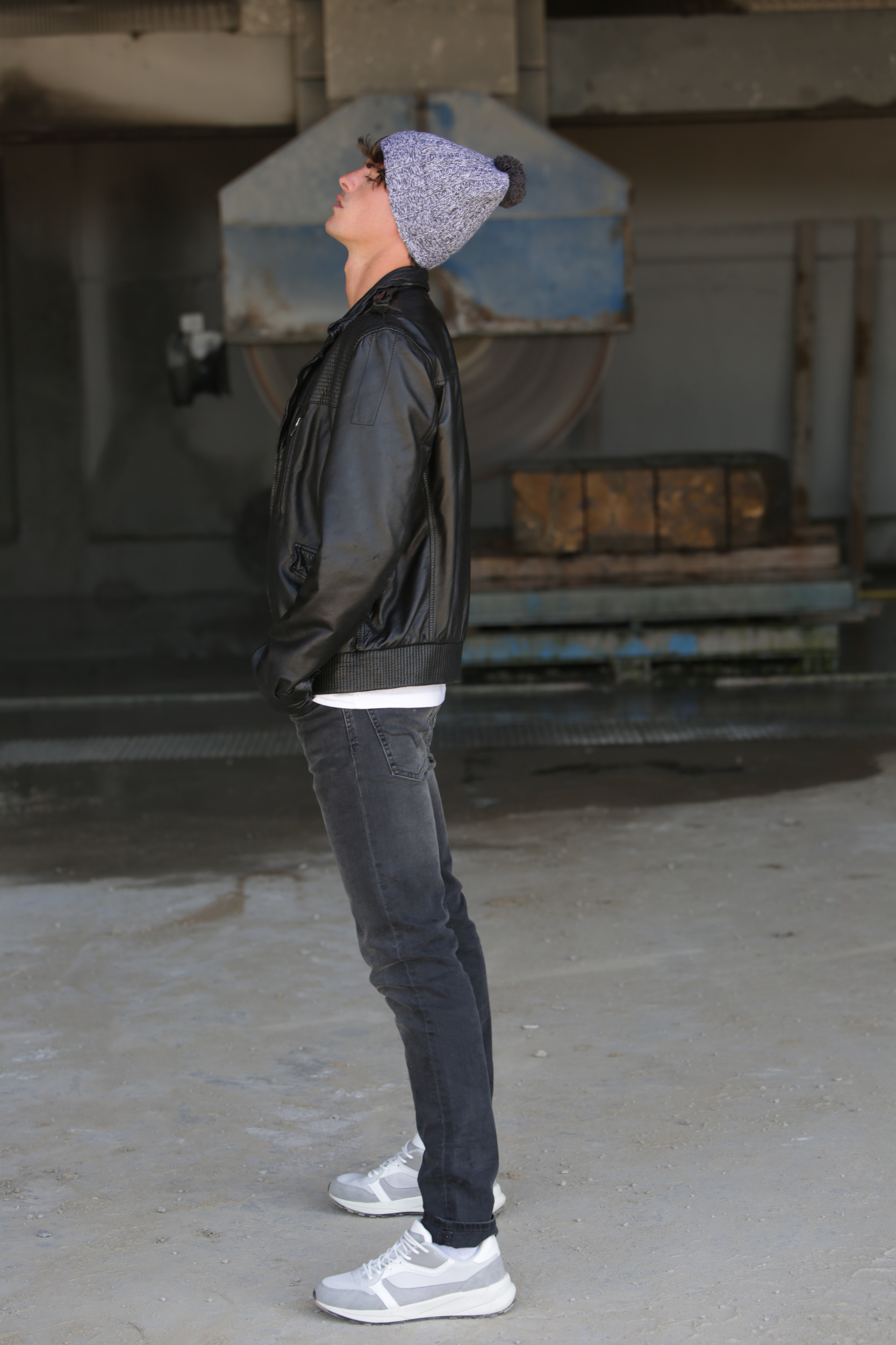 joven con gorro de punto y cazadora de cuero mirando al techo en un taller industrial