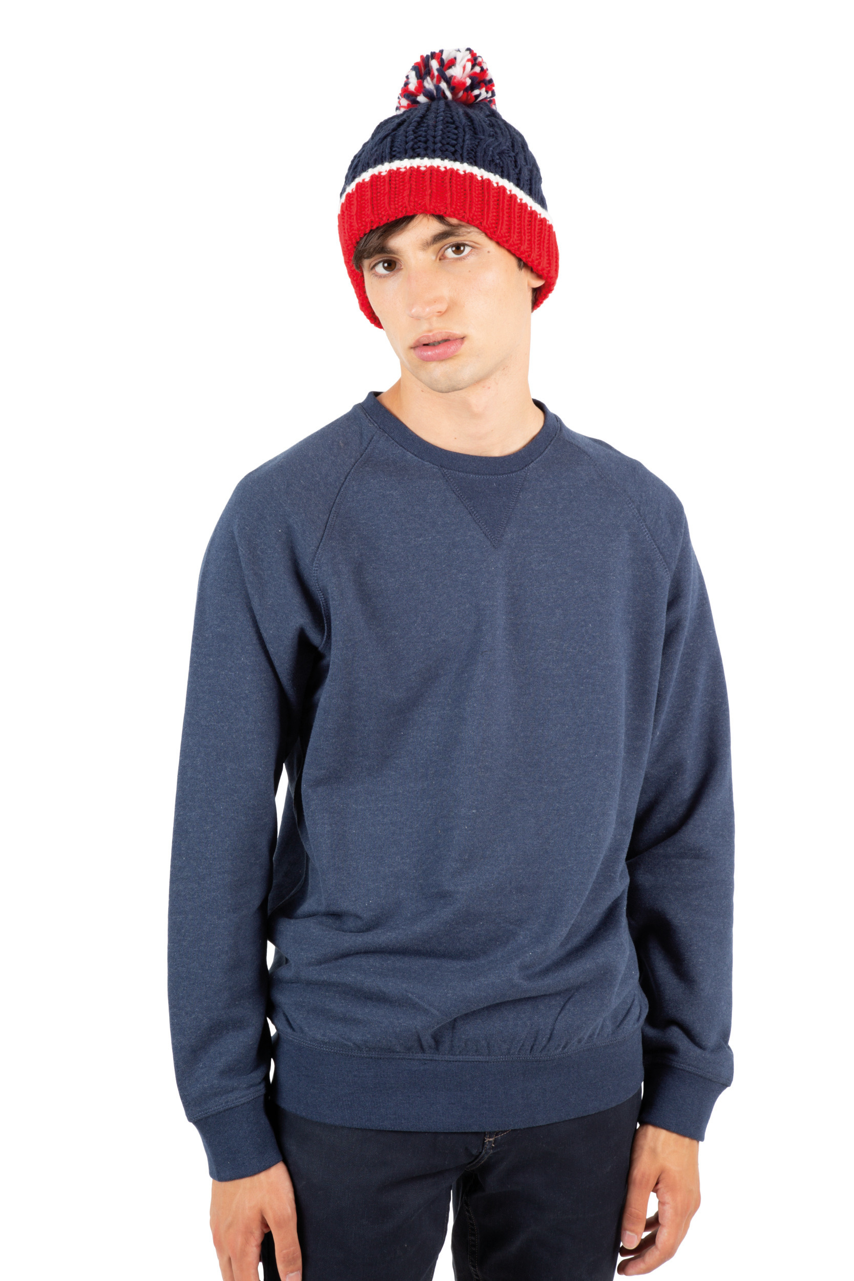 Hombre joven con gorro de lana rojo y azul y sudadera azul marino sobre fondo blanco.