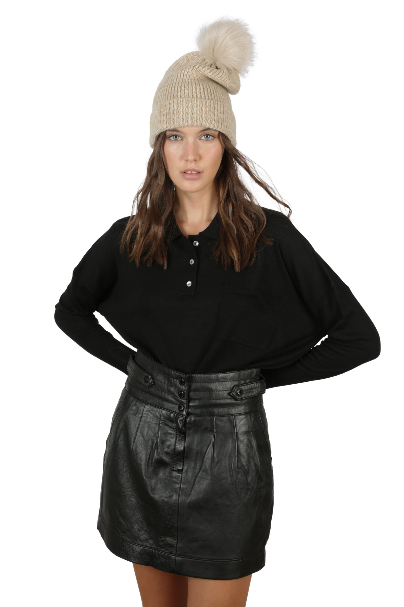 Mujer con gorro de punto beige con pompón, jersey negro de manga larga y falda corta de cuero negro sobre fondo blanco.