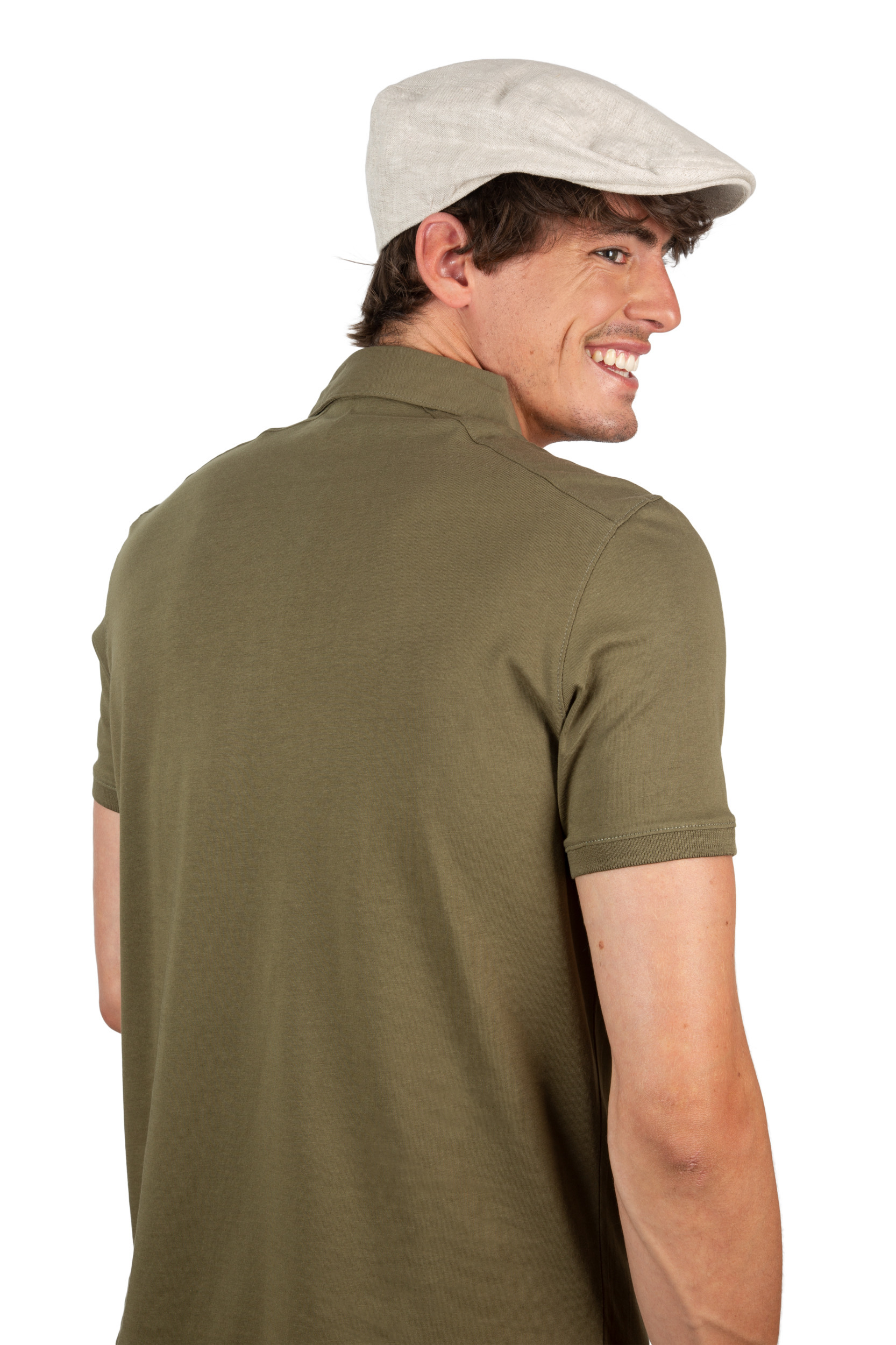 Hombre de espaldas con polo verde oliva y gorra plana beige, girando la cabeza y sonriendo.