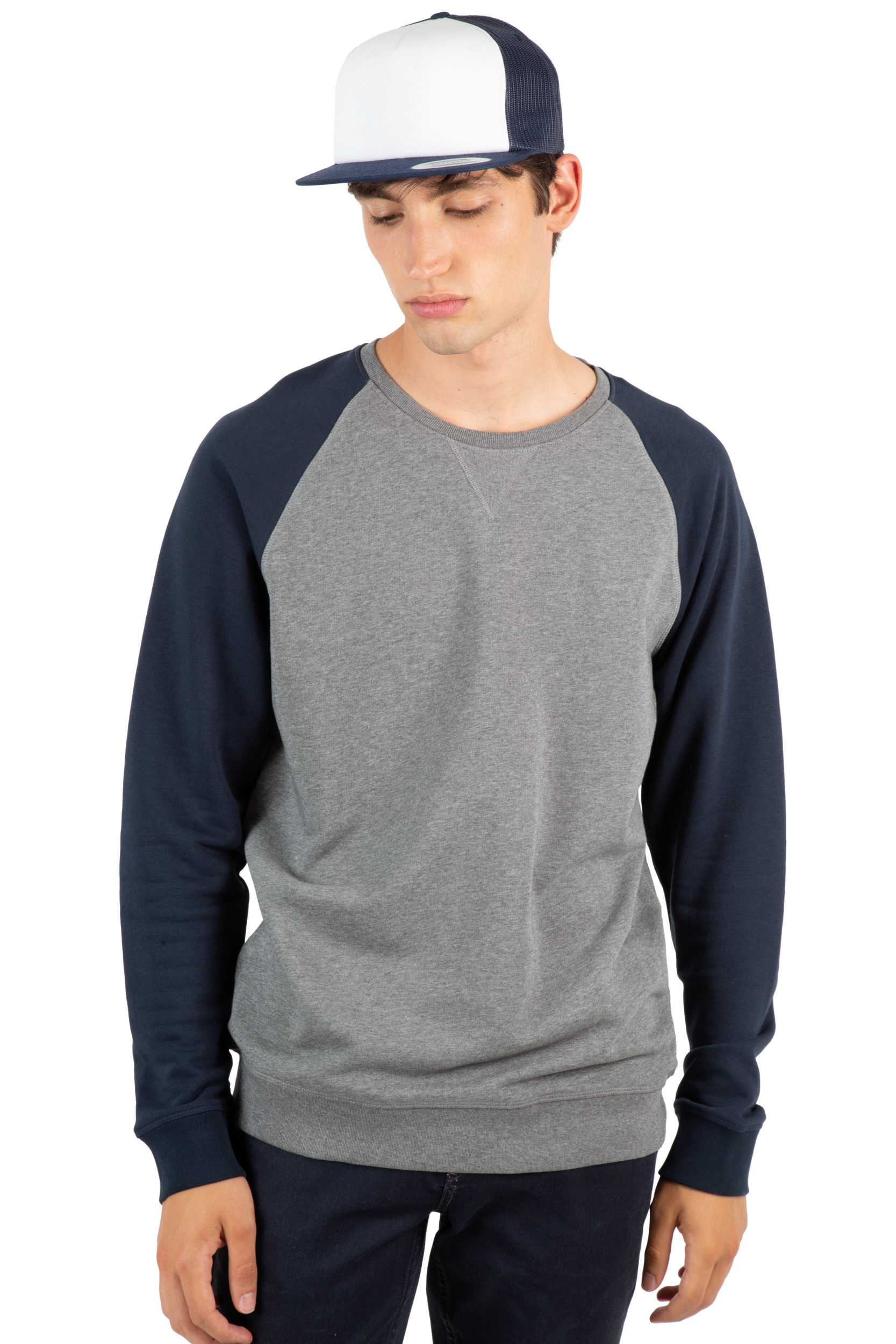 Hombre joven con sudadera gris de mangas azul marino y gorra de visera blanca mirando hacia abajo