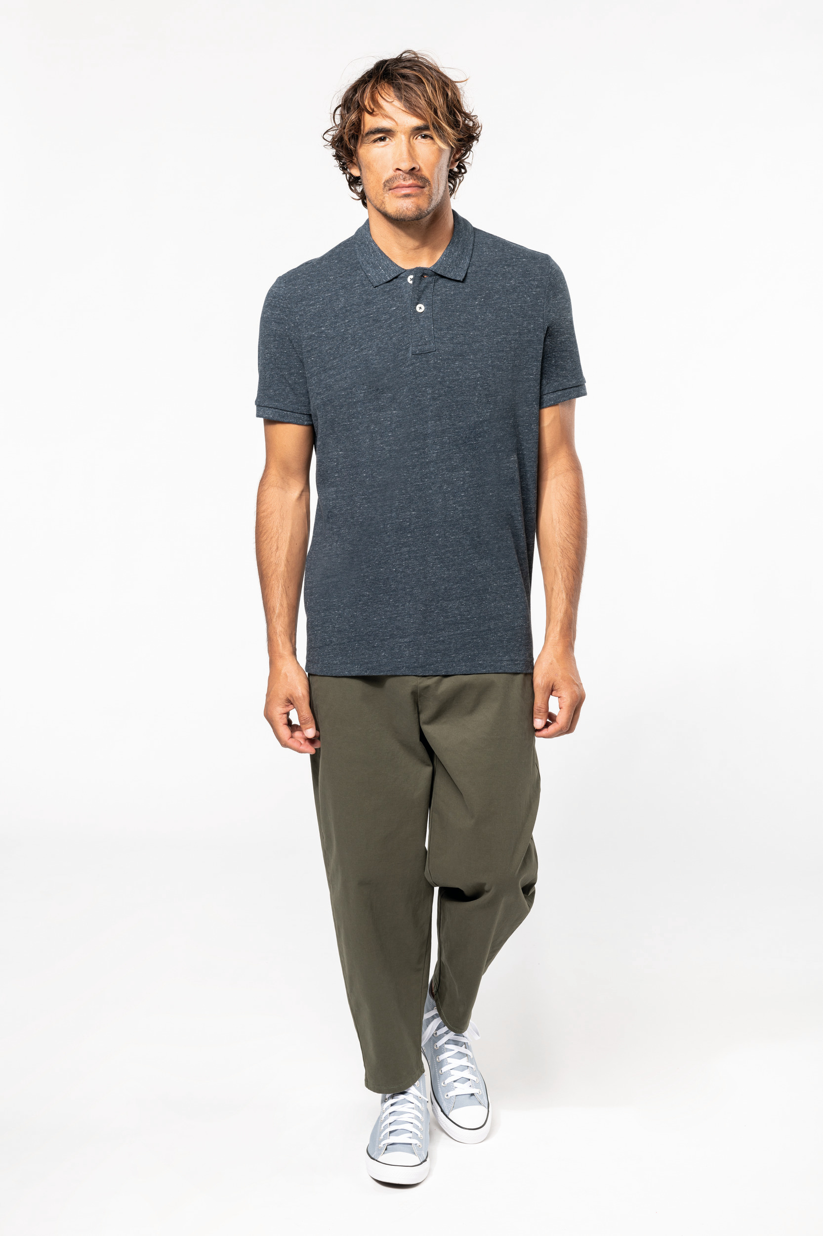 hombre con polo azul marino, pantalón verde caqui holgado y zapatillas grises sobre fondo blanco